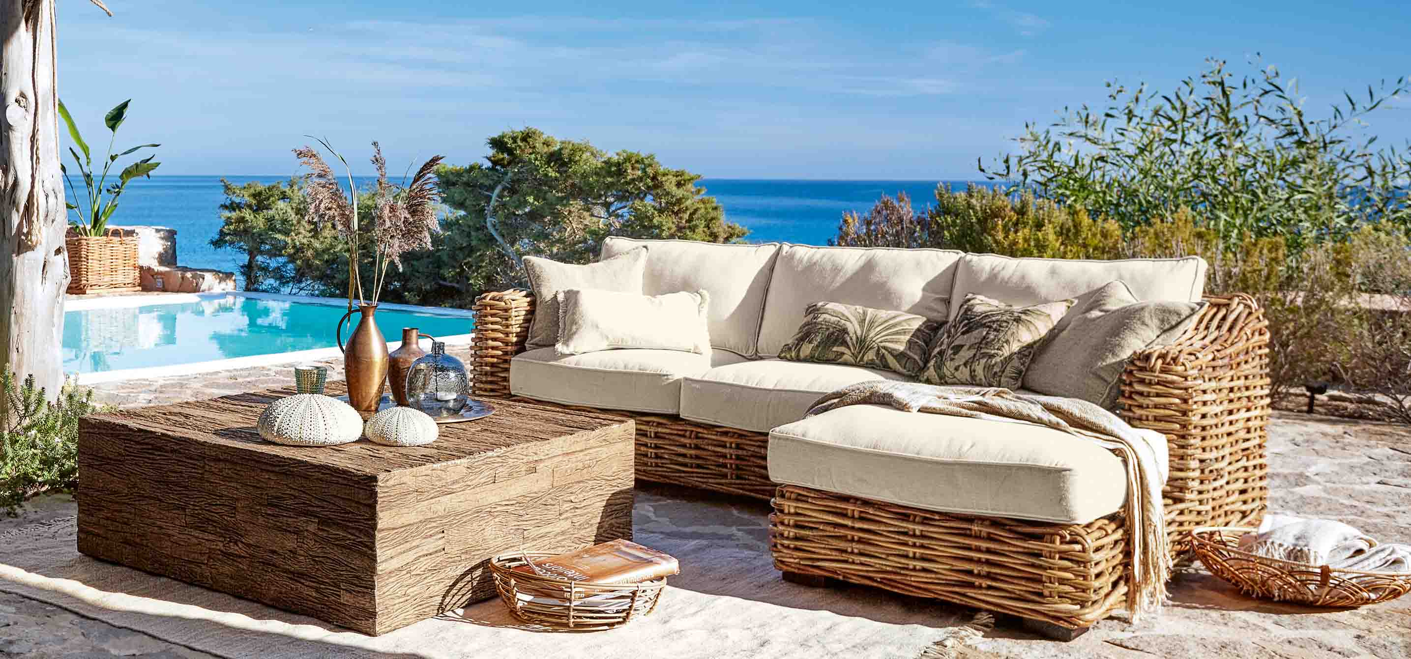 Ensemble de meubles d'extérieur en rotin avec coussins crème près d'une piscine avec vue sur la mer