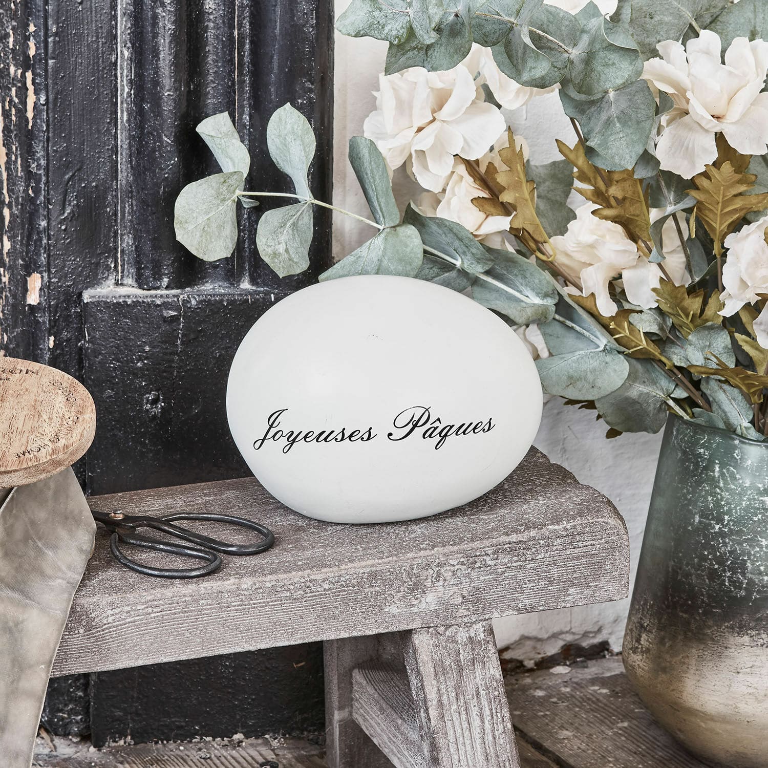 Œuf décoratif JOYEUSES PAQUES Œuf décoratif blanc avec inscription Joyeuses Pâques sur banc en bois avec fleurs et ciseaux