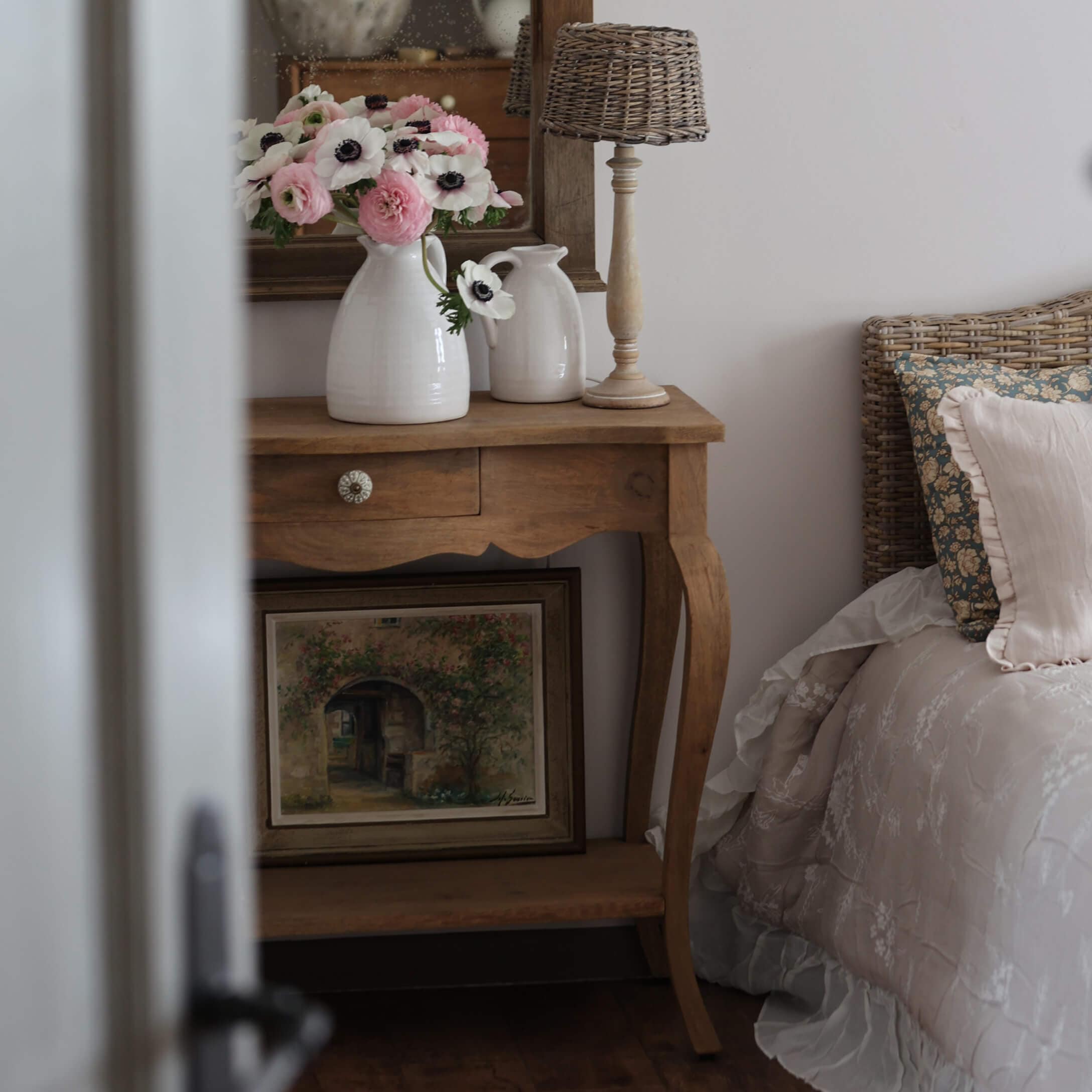 Table en bois avec vases en céramique blanche et fleurs à côté d'un lit avec tête de lit en osier