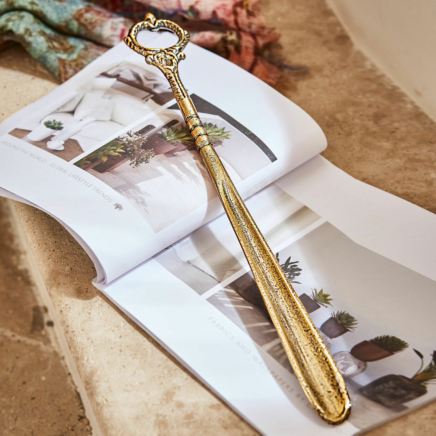 Chausse-pied Lucas Chausse-pied en métal doré avec poignée décorative posé sur un magazine d'intérieur ouvert