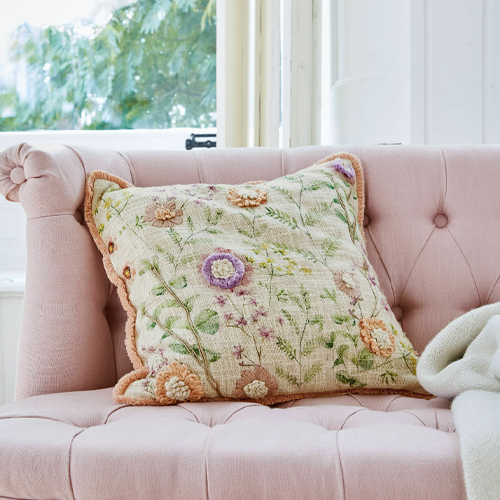Coussin décoratif brodé de fleurs pastel sur un canapé rose, tissu doux et confortable