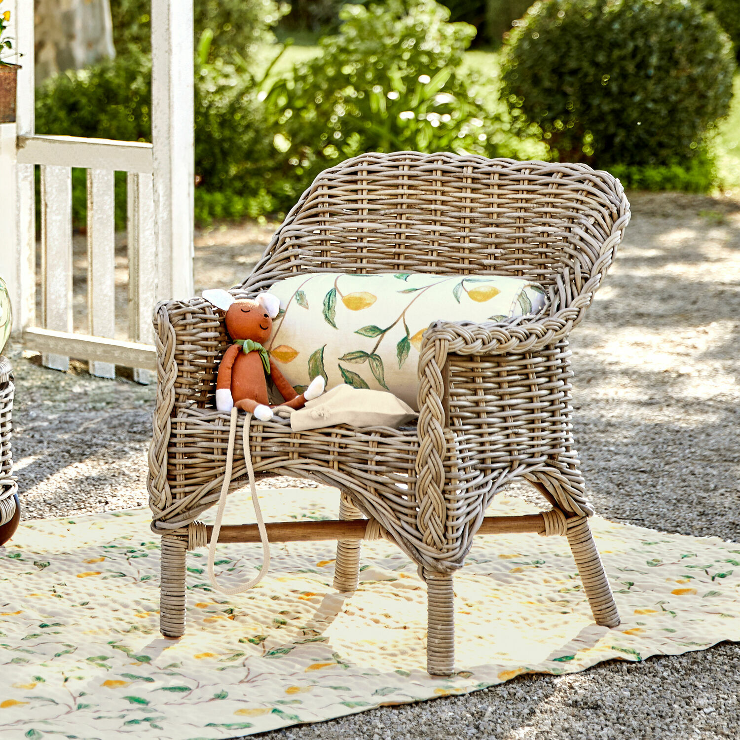 Fauteuil pour enfant Narivena Fauteuil en rotin naturel avec coussin à motif feuilles et peluche dans un jardin ensoleillé