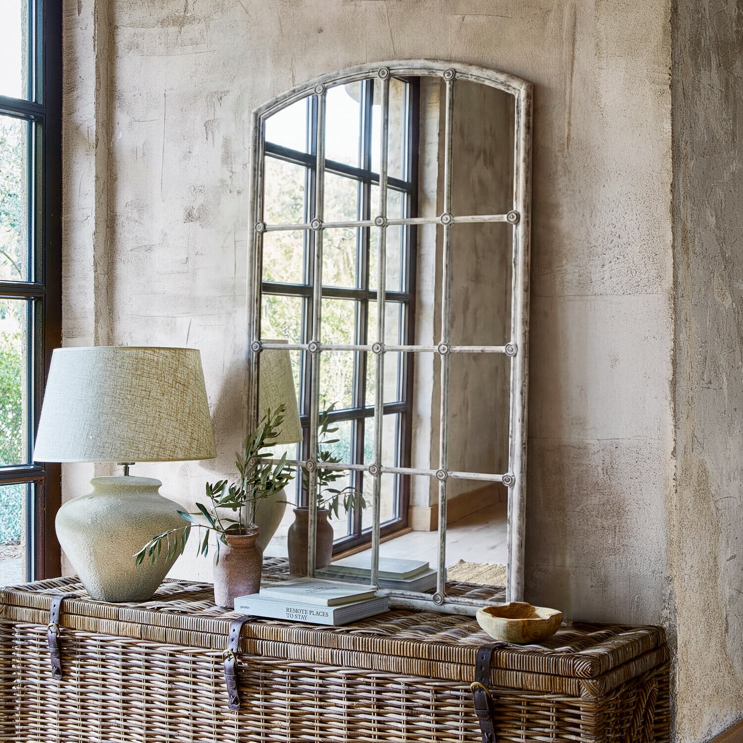 Miroir Tobiah Miroir à cadre blanc vieilli sur commode en osier avec lampe et plante décorative dans un intérieur rustique