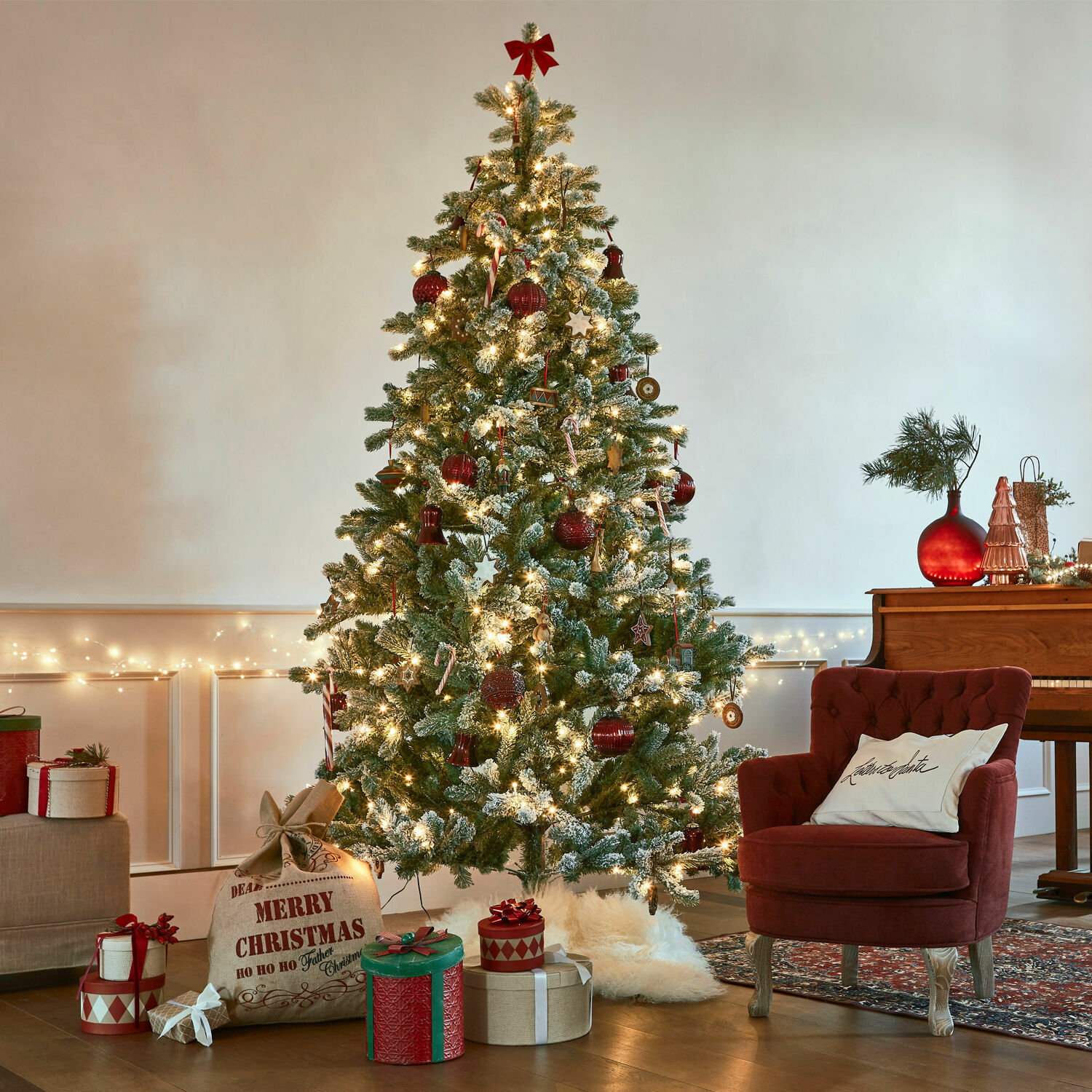 Sapin de Noël Mannier Sapin de Noël artificiel enneigé décoré de boules rouges et guirlandes lumineuses dans un salon chaleureux