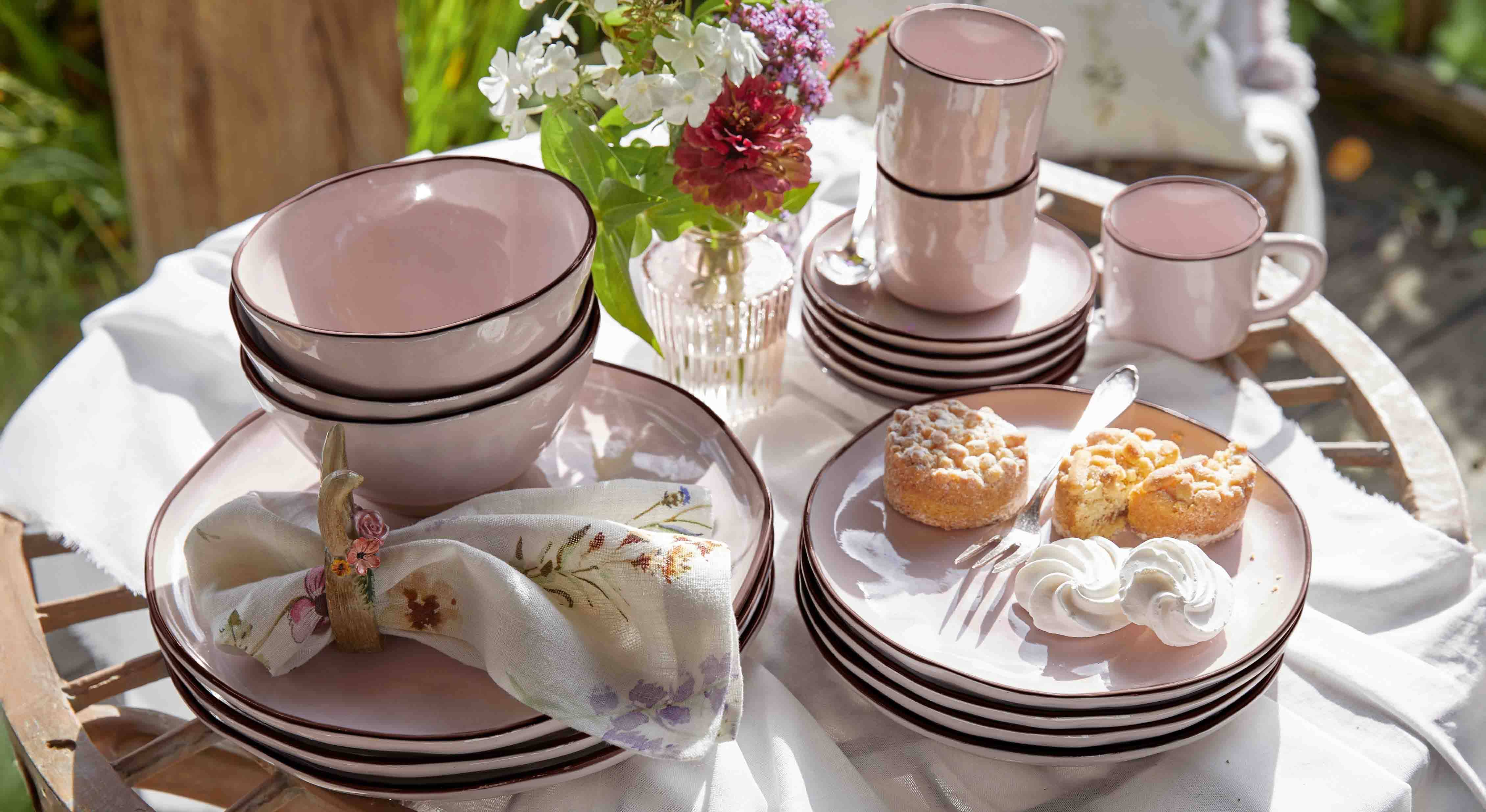 Service de vaisselle en céramique rose avec assiettes, bols et tasses sur table en bois avec gâteaux et fleurs