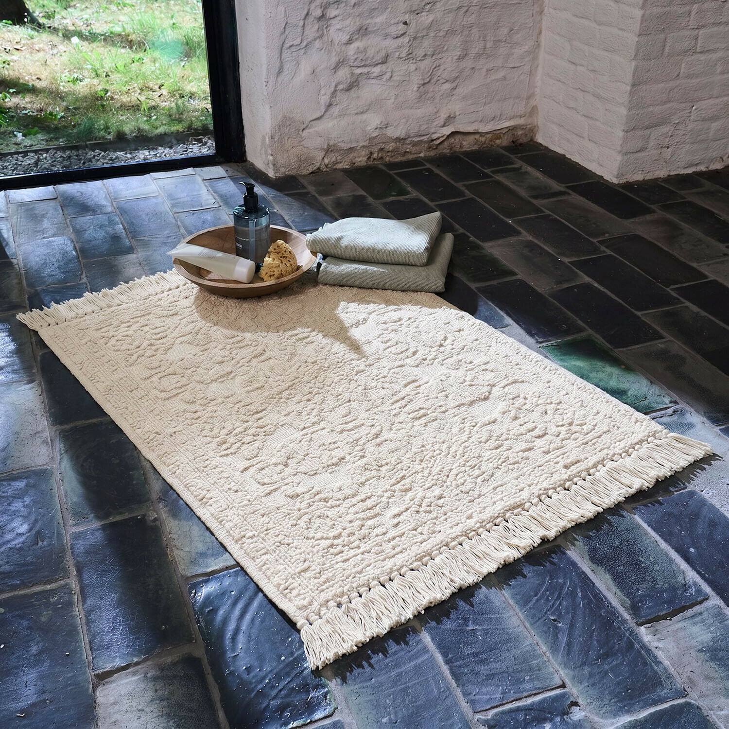 Vase 2er Set Dolcin Tapis crème en coton avec franges sur sol en pierre sombre avec accessoires de salle de bain