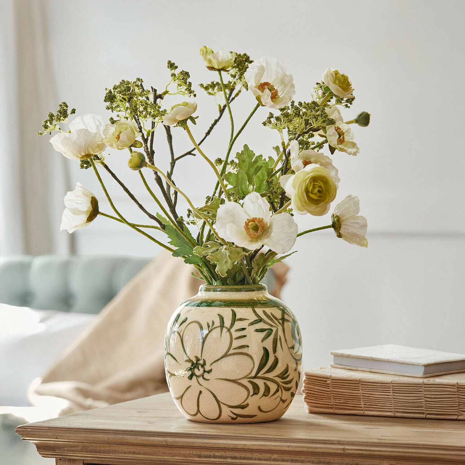 Vase en céramique beige avec motifs floraux verts et fleurs blanches artificielles sur table en bois