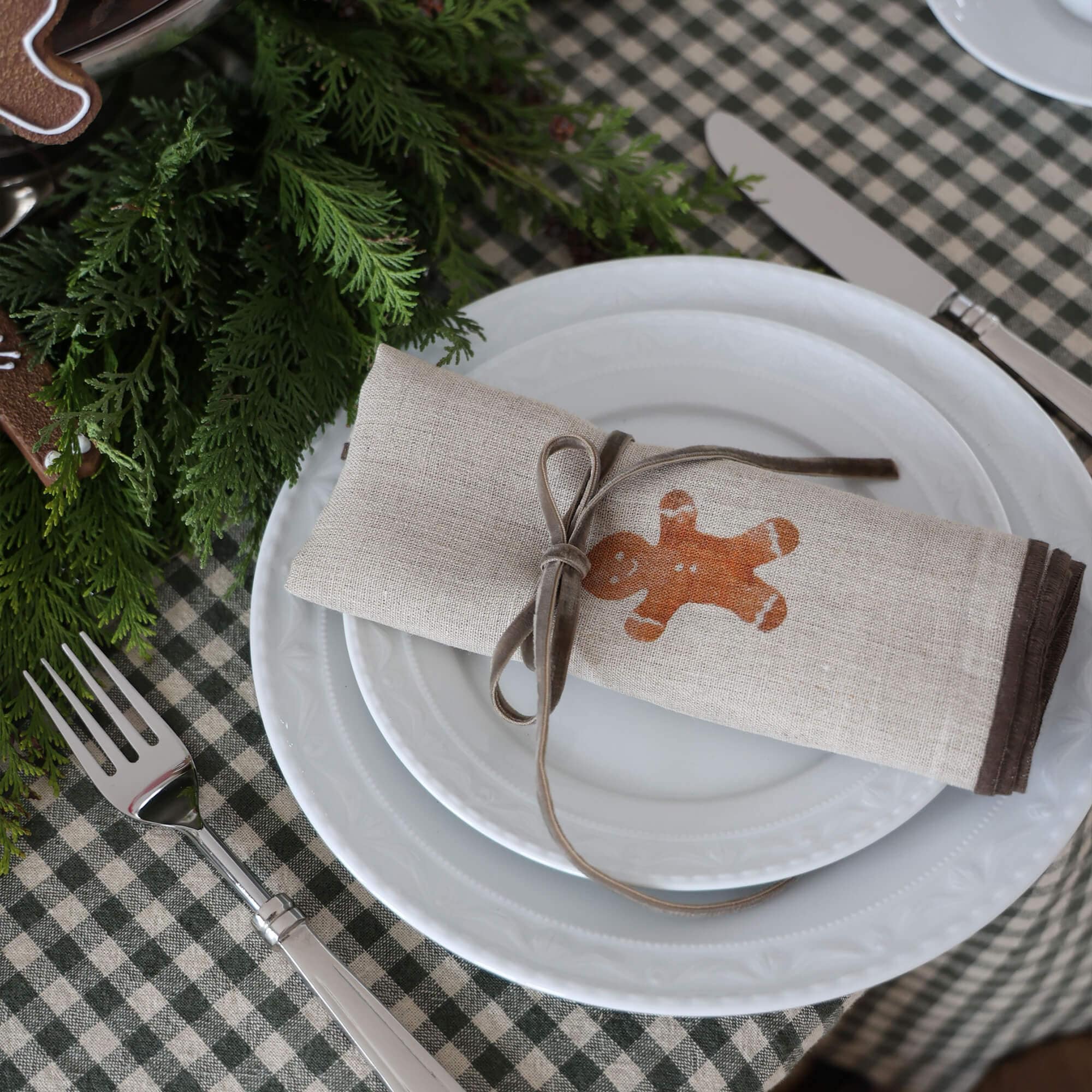 Serviette en lin beige avec motif bonhomme en pain d'épice et ruban gris sur assiette blanche