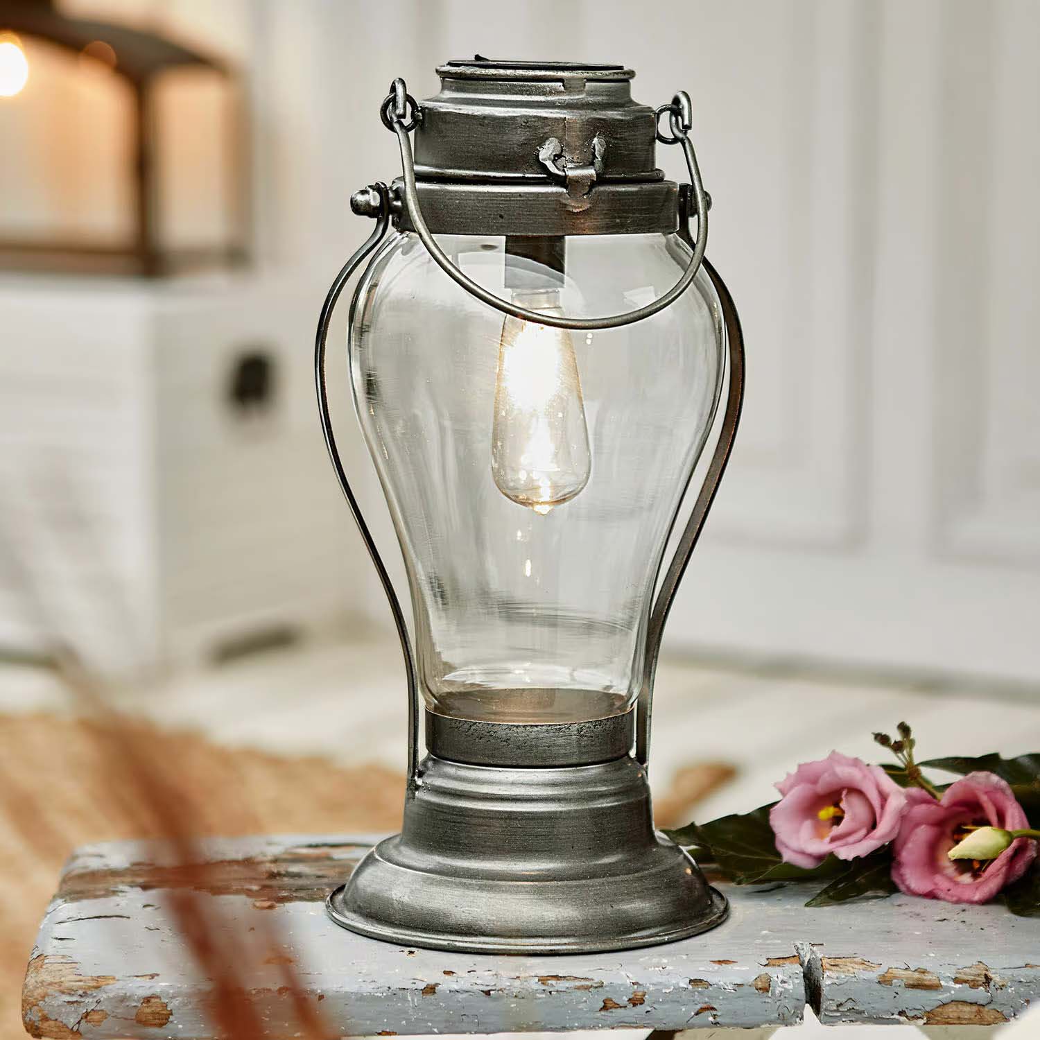Lanterne en métal avec abat-jour en verre transparent et ampoule allumée sur une table rustique