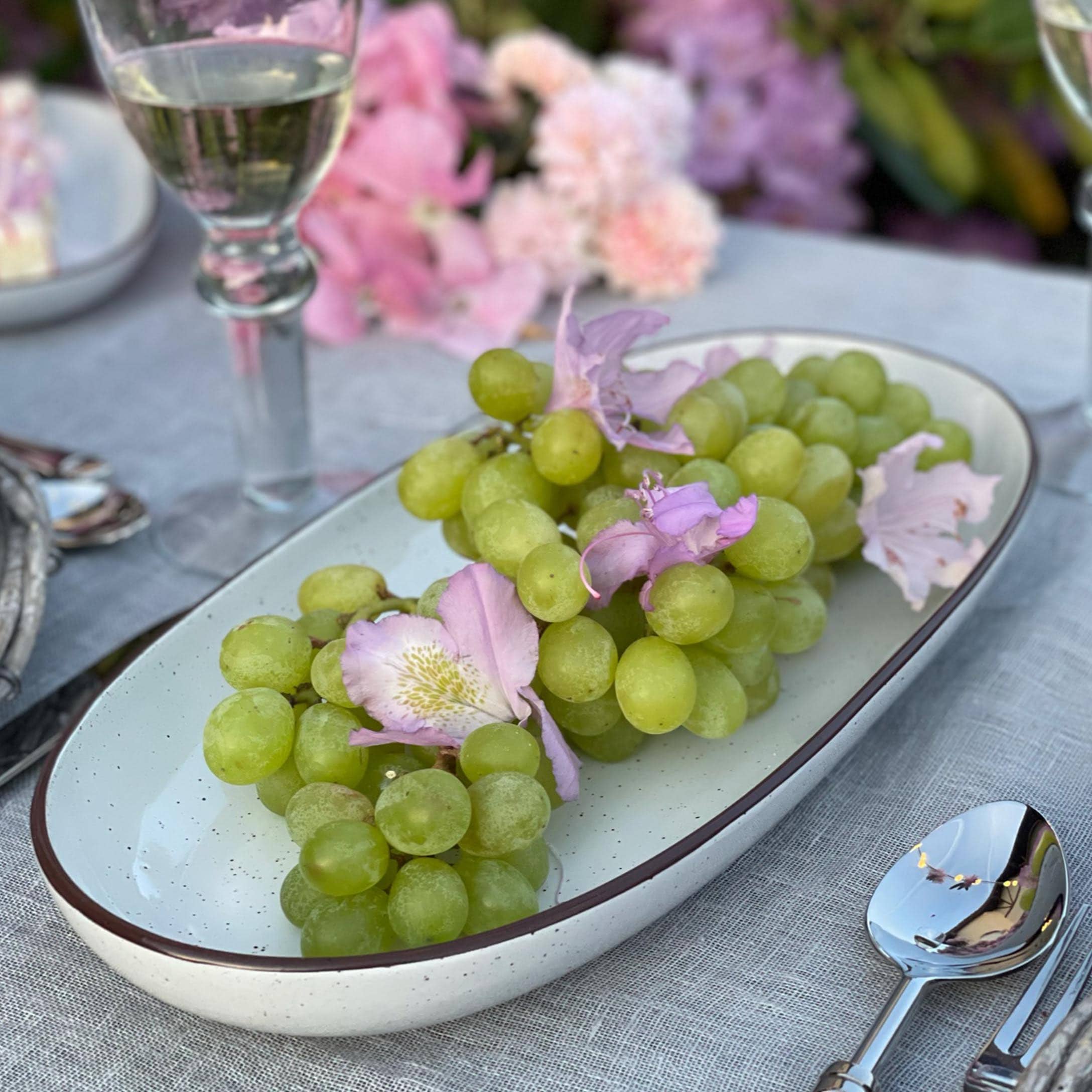 Raisins verts avec fleurs roses sur une assiette en céramique blanche posée sur une nappe grise