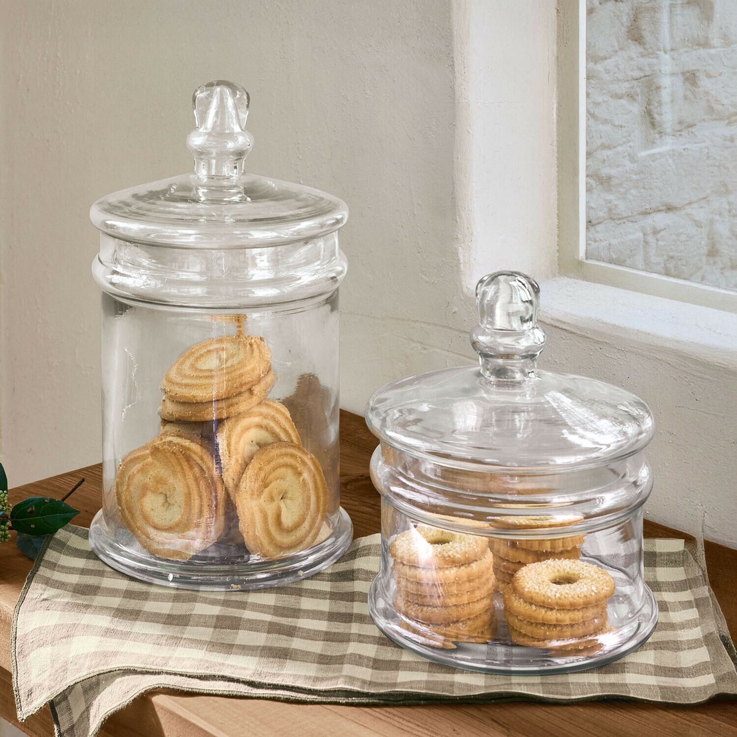Deux bocaux en verre transparents avec couvercles remplis de biscuits sur une table en bois à carreaux