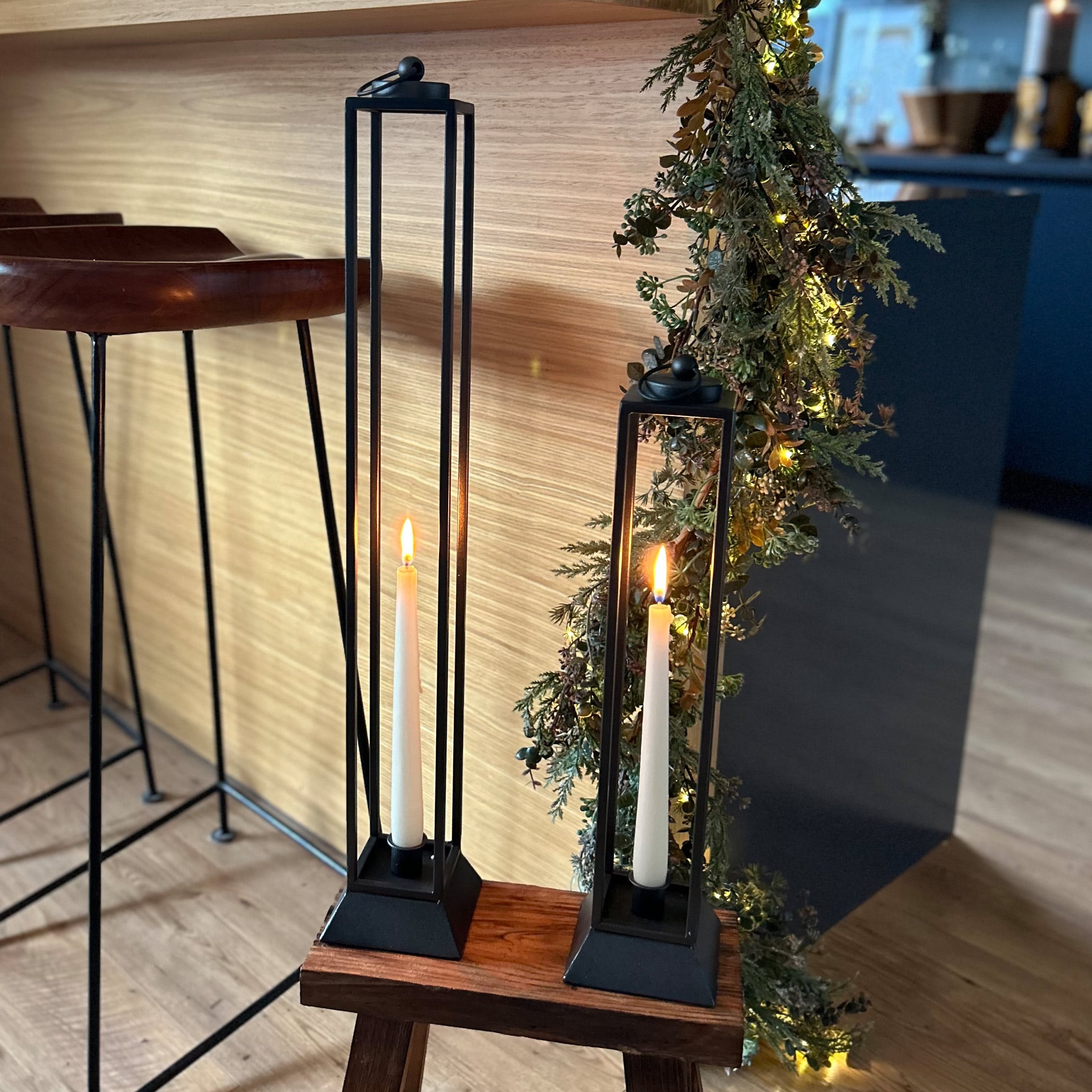Deux bougeoirs en métal noir avec bougies blanches sur un tabouret en bois dans un intérieur moderne