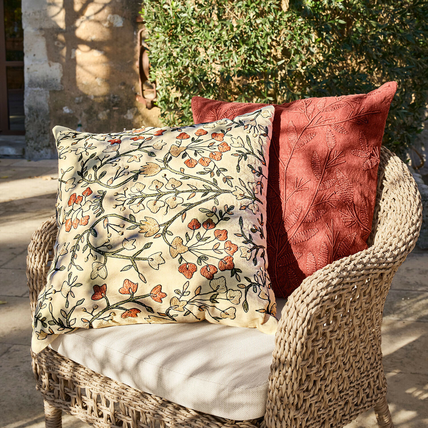 Deux coussins décoratifs brodés de motifs floraux et feuillages sur fauteuil en osier en extérieur