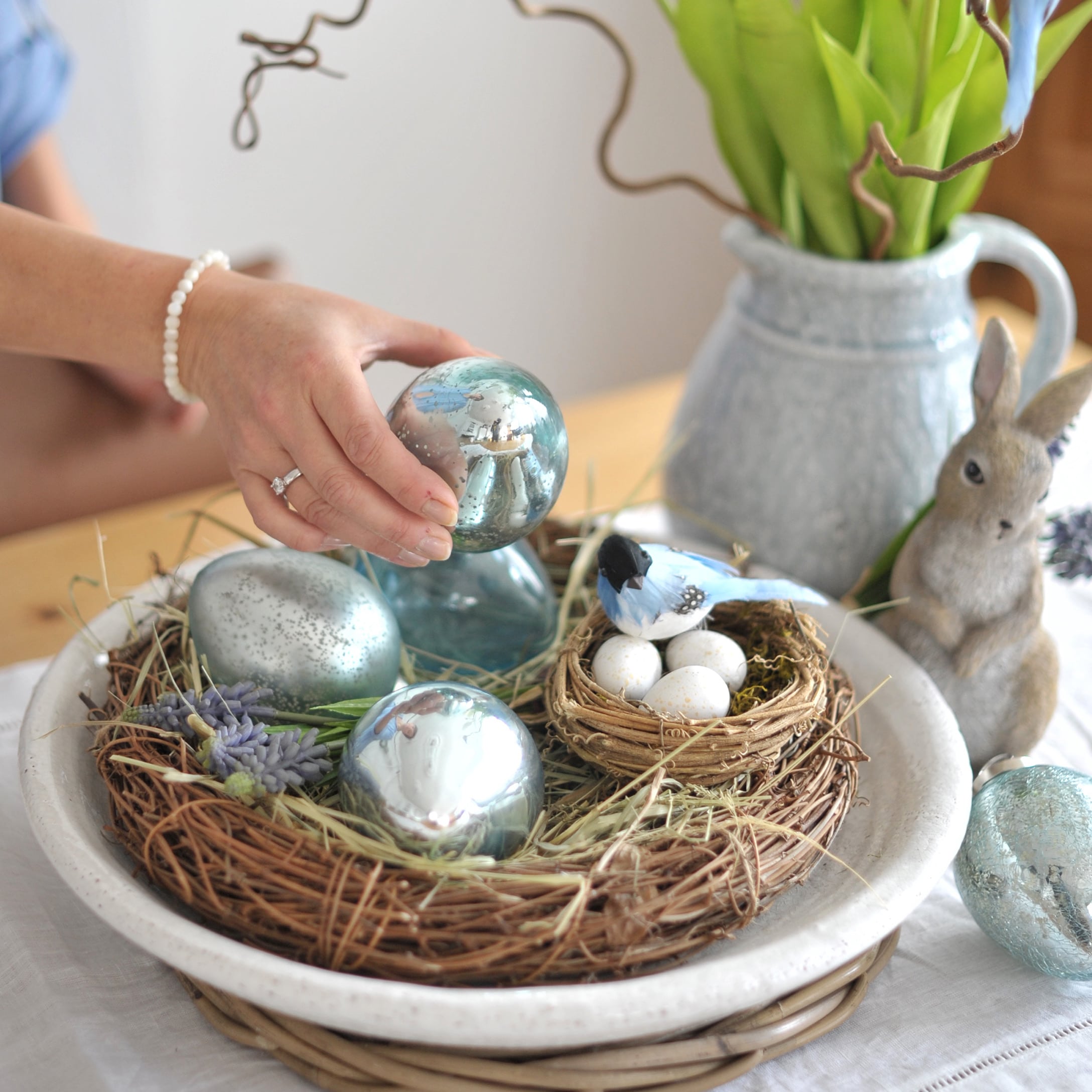 Décoration de Pâques avec œufs en verre bleus et nid avec œufs blancs sur une table en bois