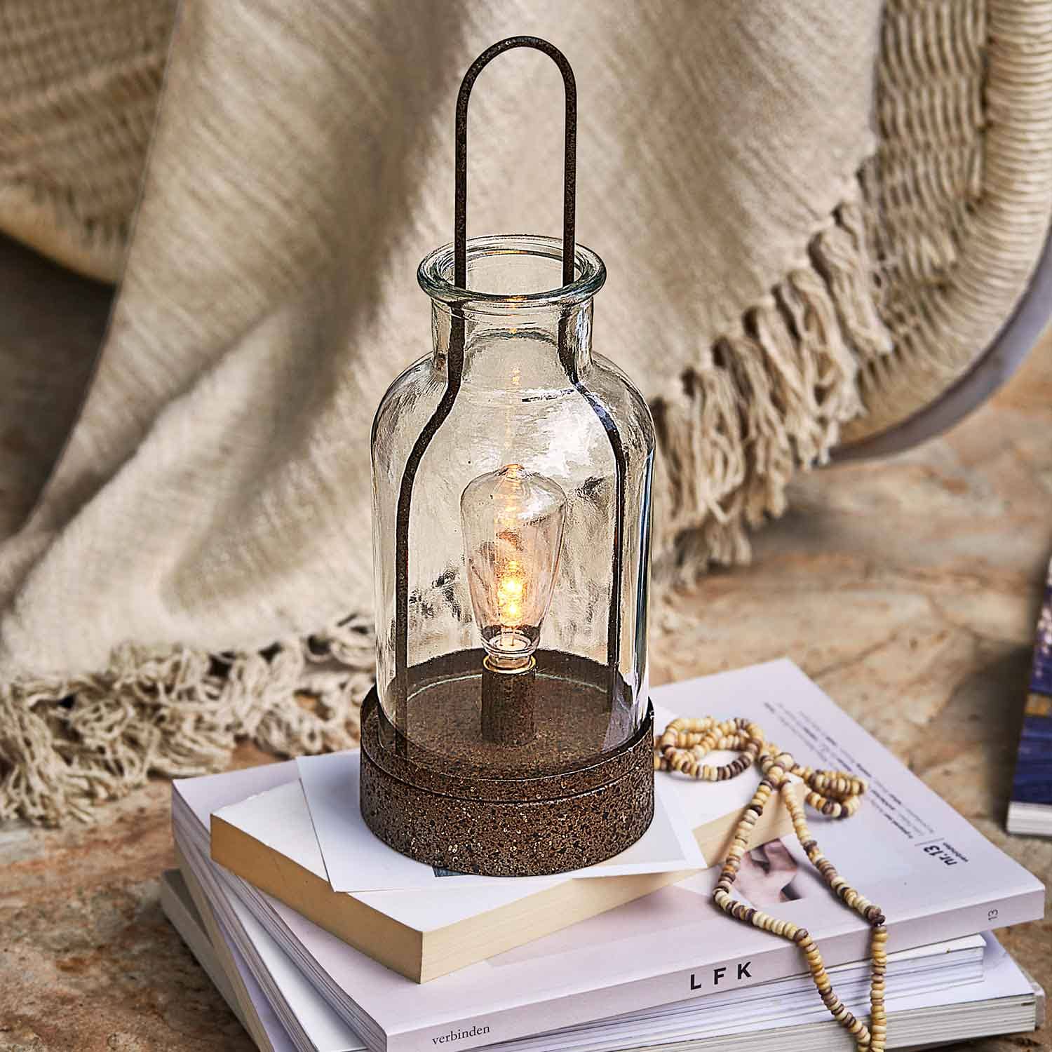 Lanterne en verre avec base métallique rouillée posée sur des livres, décoration intérieure et éclairage