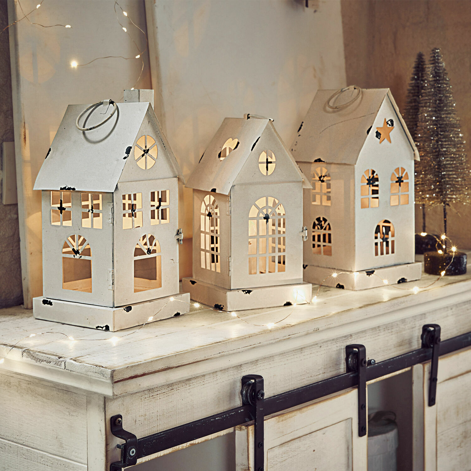 Lot de 3 lanternes LED Village Ensemble de trois lanternes en métal blanc en forme de maison avec fenêtres découpées et éclairage festif