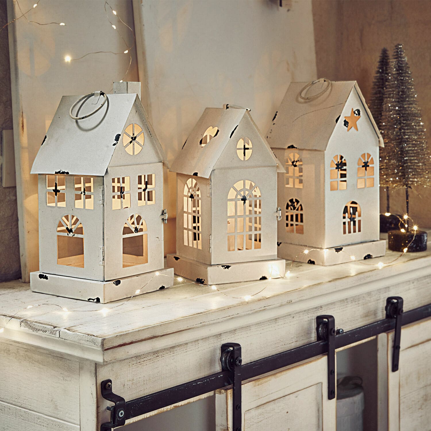 Lot de 3 lanternes LED Village Ensemble de trois lanternes en métal blanc en forme de maison avec fenêtres découpées et éclairage festif