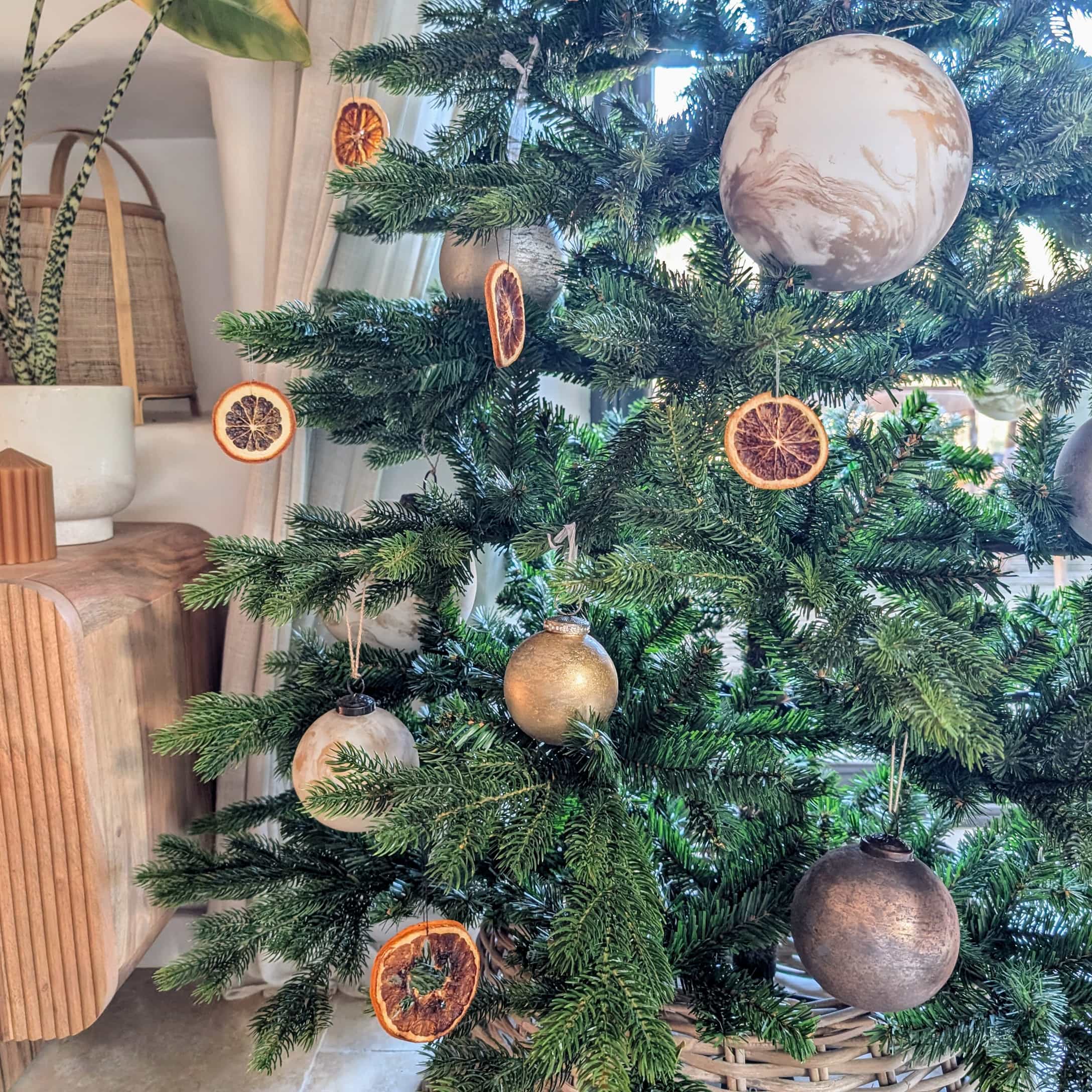 Sapin vert décoré de tranches d'orange séchées naturelles et de boules dorées et beige pour Noël.