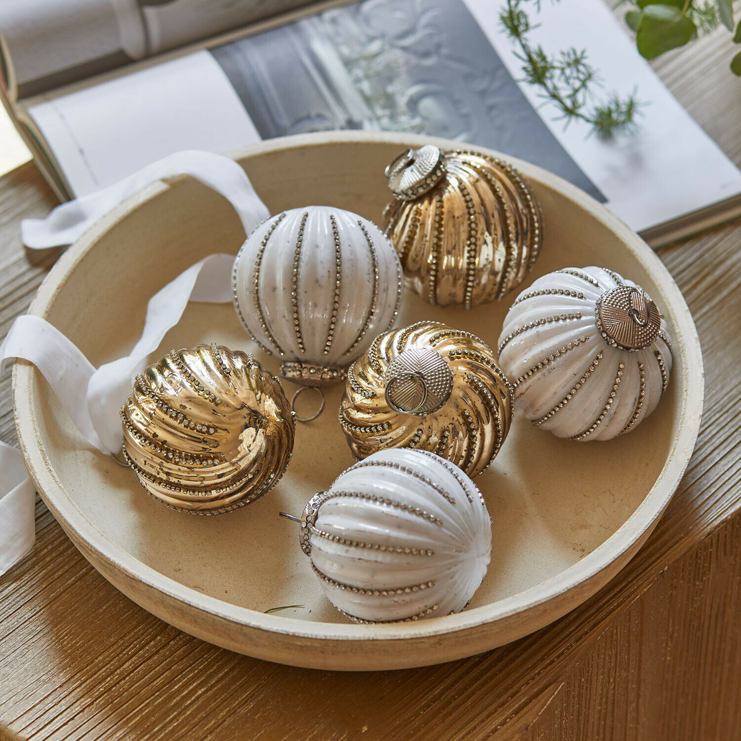 Boule de nuit molle, set de 6 Shaela Ensemble de boules de Noël blanches et dorées avec finition métallique dans un bol rond sur une table en bois