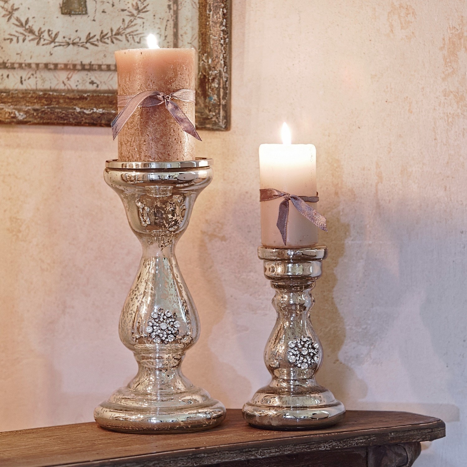 Lot de 2 bougeoirs Lysiane Deux bougeoirs argentés avec cristaux décoratifs et bougies beige nouées de rubans sur une table en bois