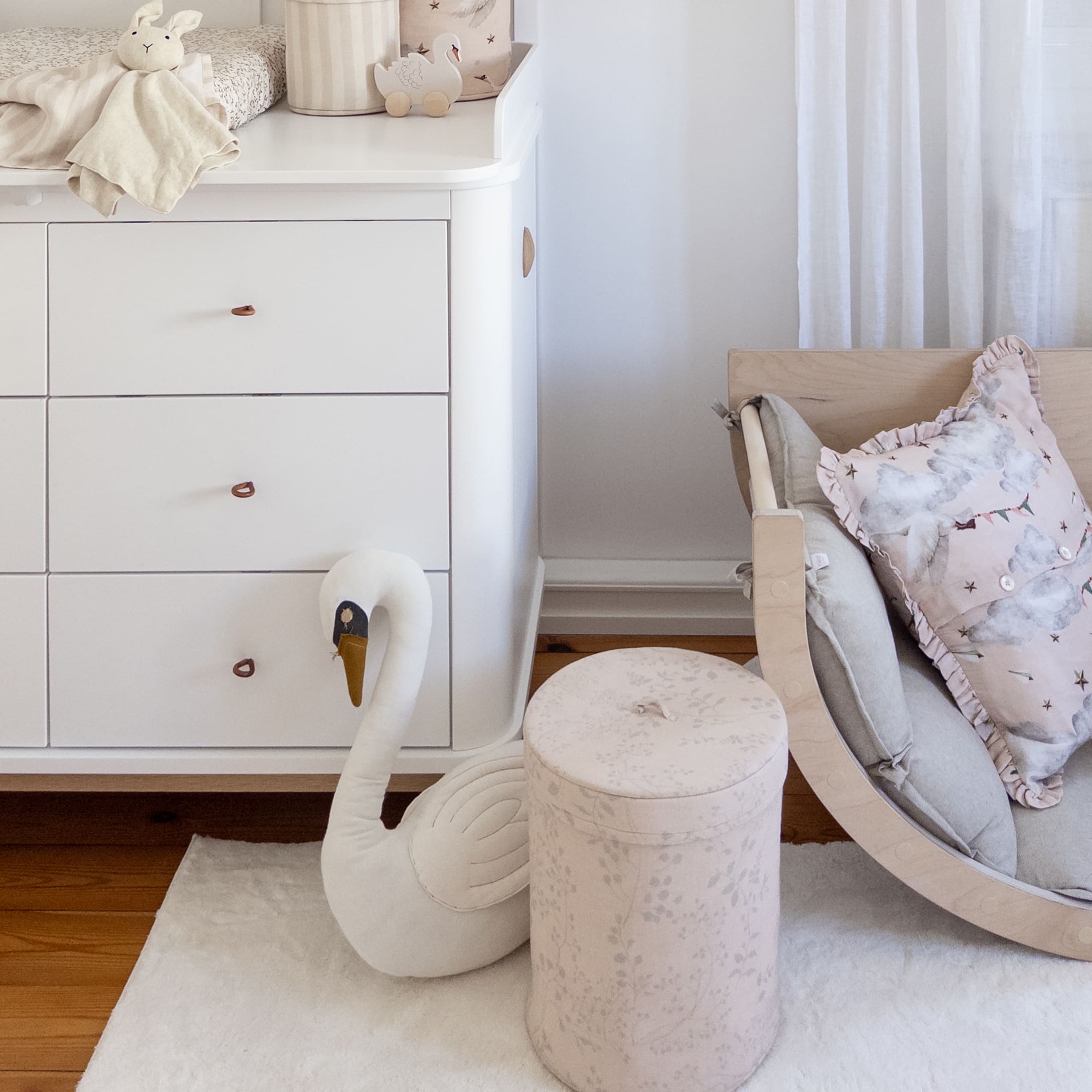 Chambre d'enfant cosy avec commode blanche, cygne en peluche et pouf rose poudré en tissu