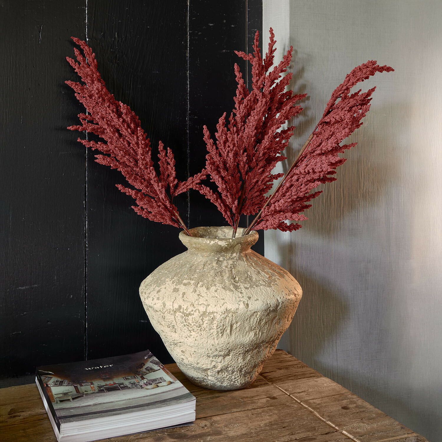 Vase Moravinos Vase en argile texturée avec branches rouges séchées sur une table en bois rustique