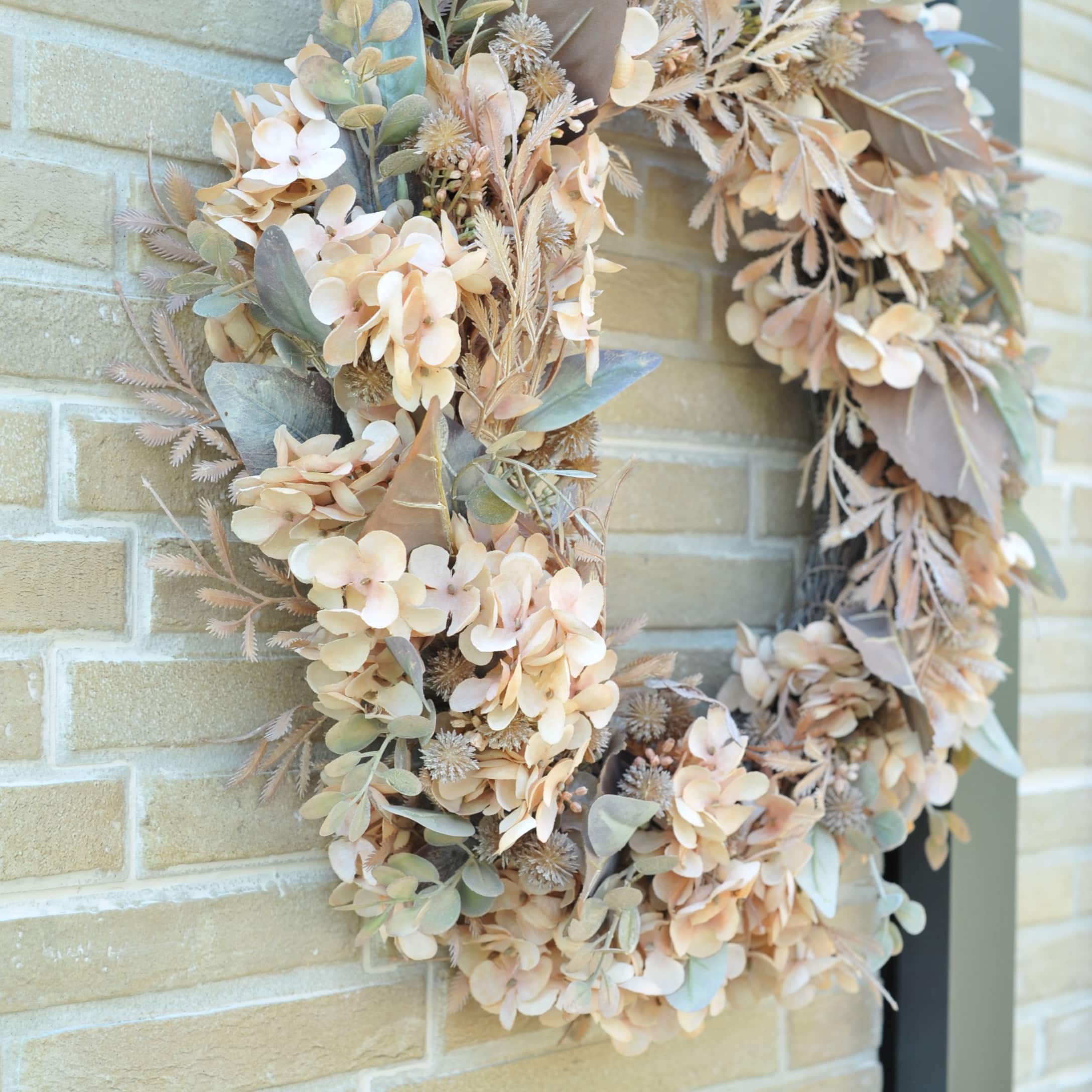 Couronne d'automne décorative en fleurs séchées beige et vertes accrochée sur un mur en briques claires