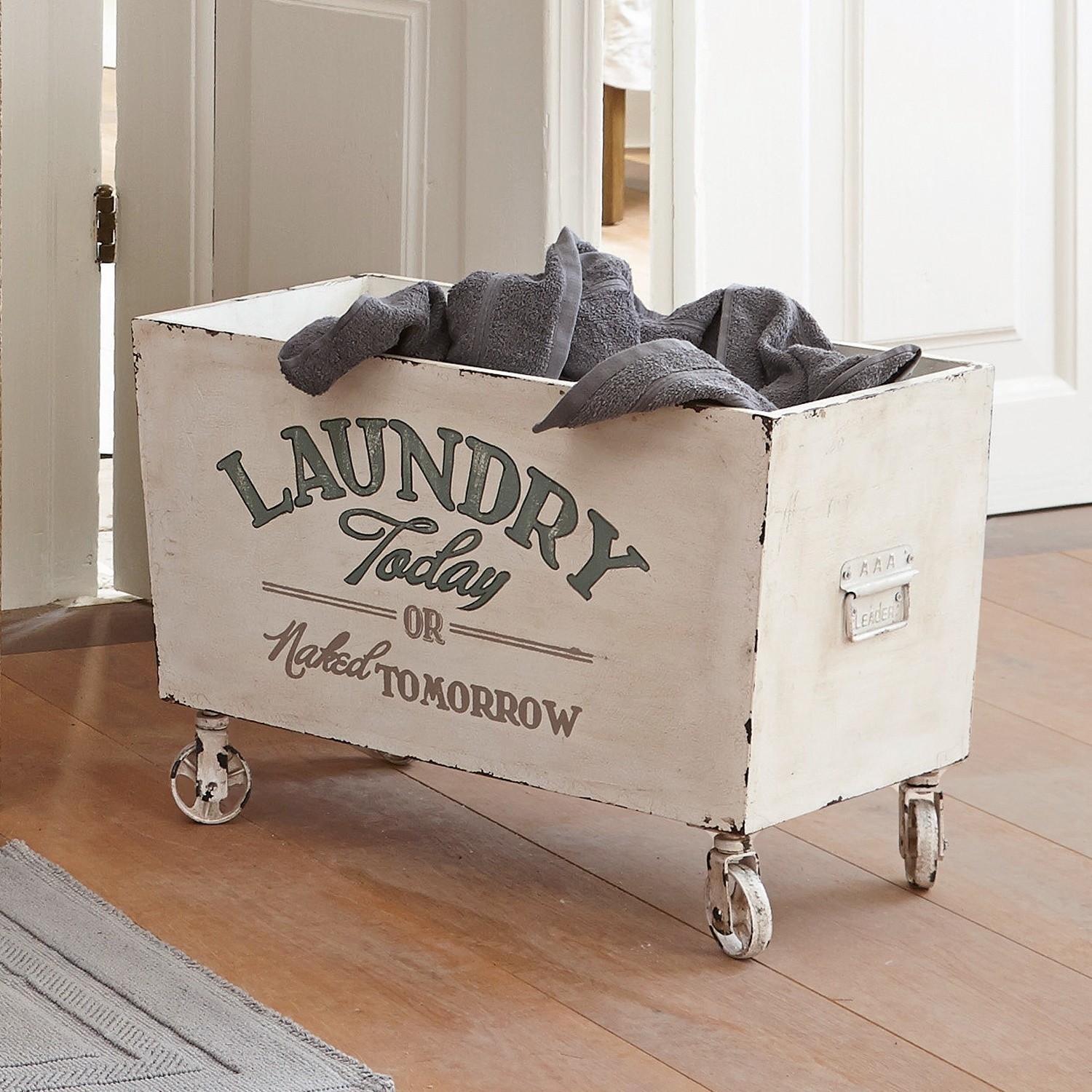 Coffre en bois Today Panier à linge en métal blanc sur roulettes avec serviettes grises dans un intérieur en bois