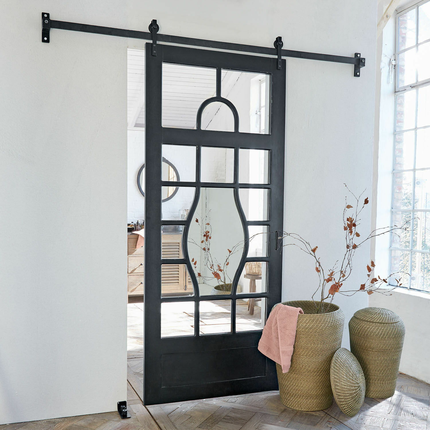 Porte coulissante Wilmorton Porte coulissante noire en métal avec miroir à motifs géométriques dans une pièce lumineuse avec paniers en osier