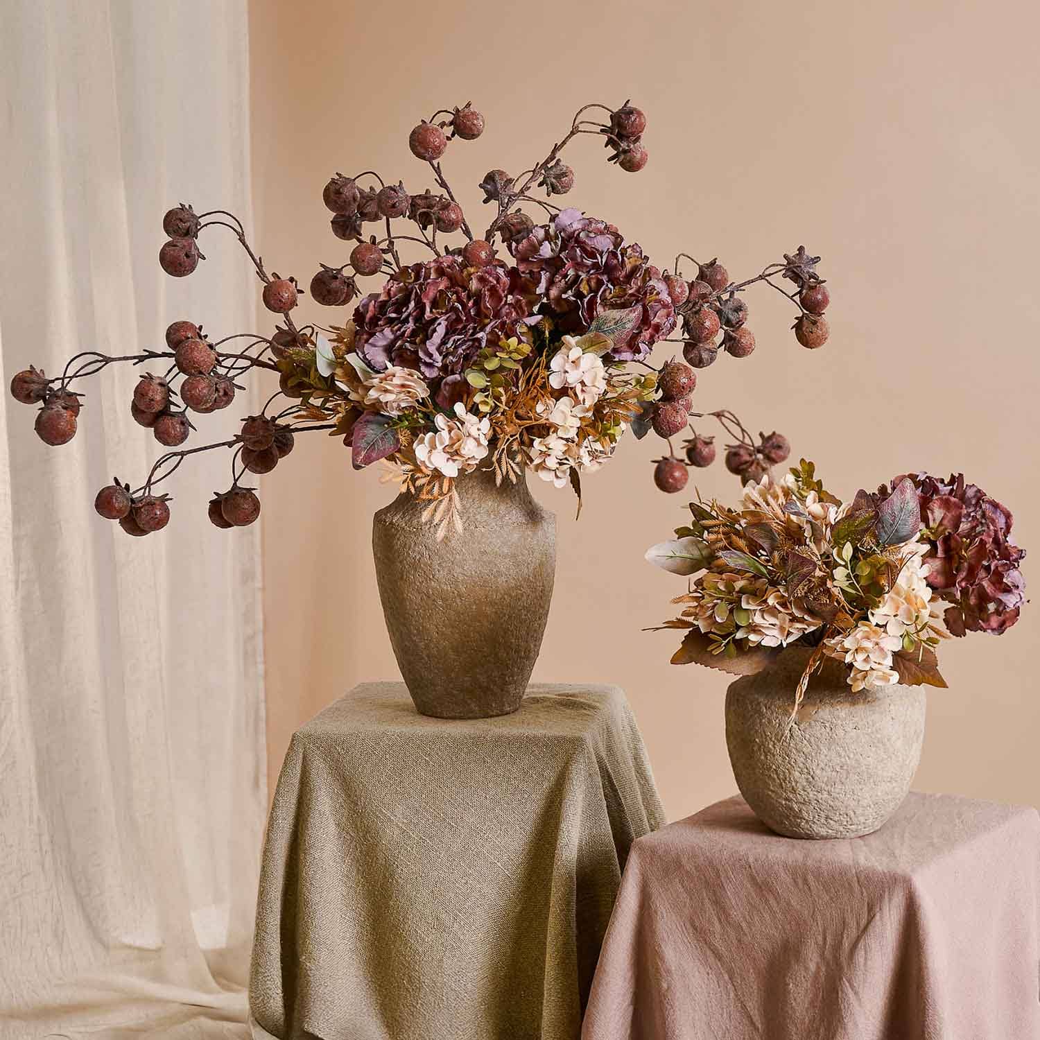 Deux bouquets décoratifs de fleurs séchées dans des vases beige sur des tables drapées de tissu