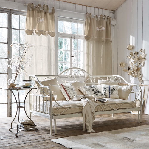 Canapé en métal blanc avec coussins beige et rideaux légers dans un salon rustique lumineux