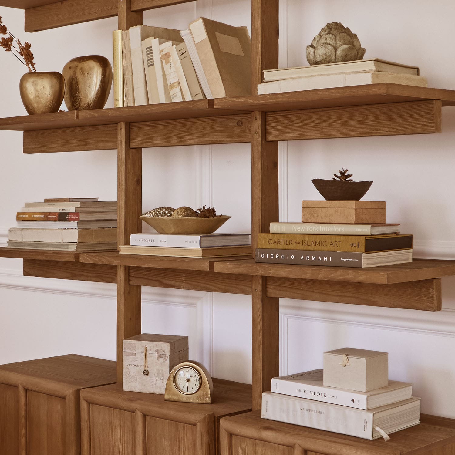 Étagère en bois avec livres, décorations dorées et horloge, ambiance élégante pour intérieur