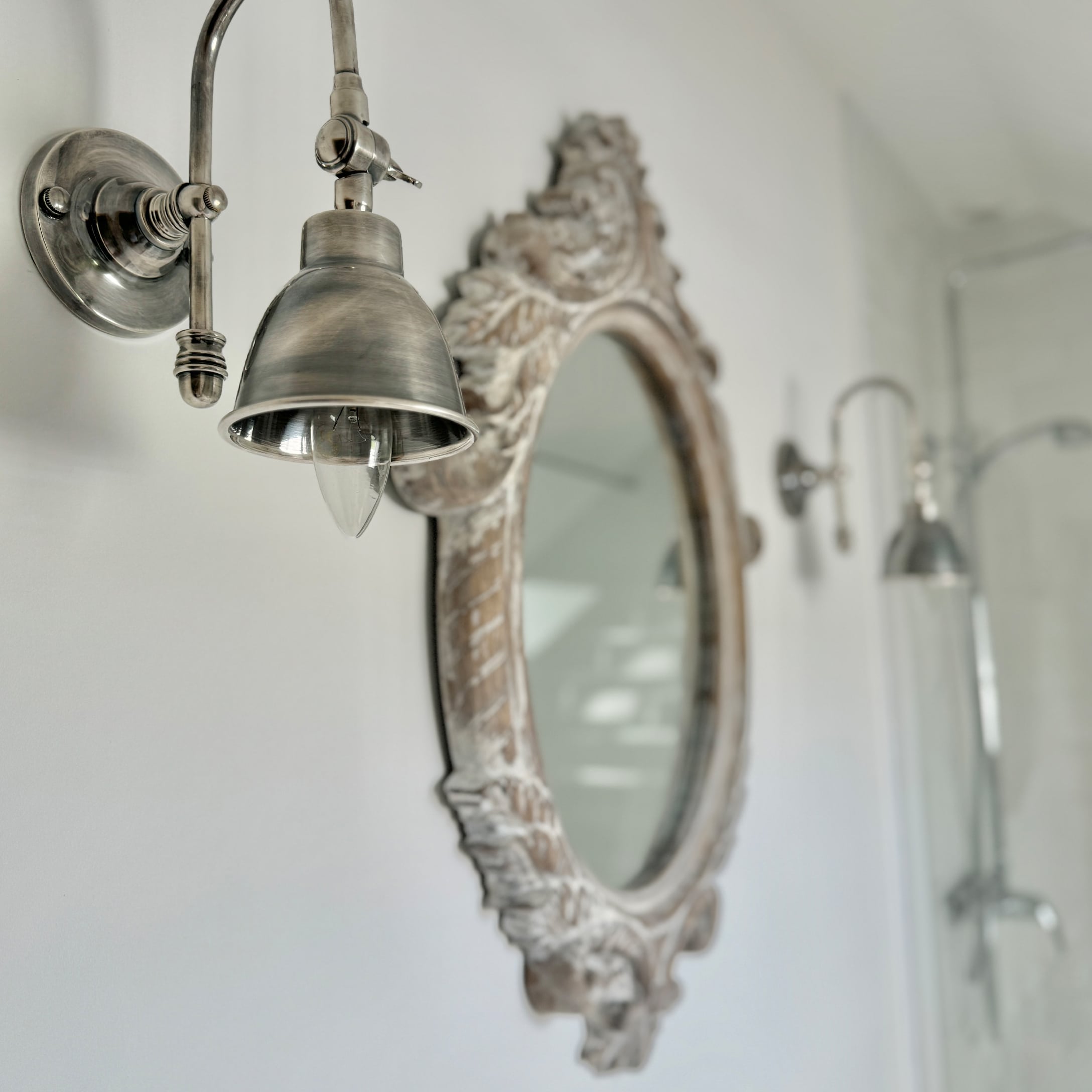 Applique murale en métal style vintage à côté d'un miroir décoratif dans une salle de bain claire