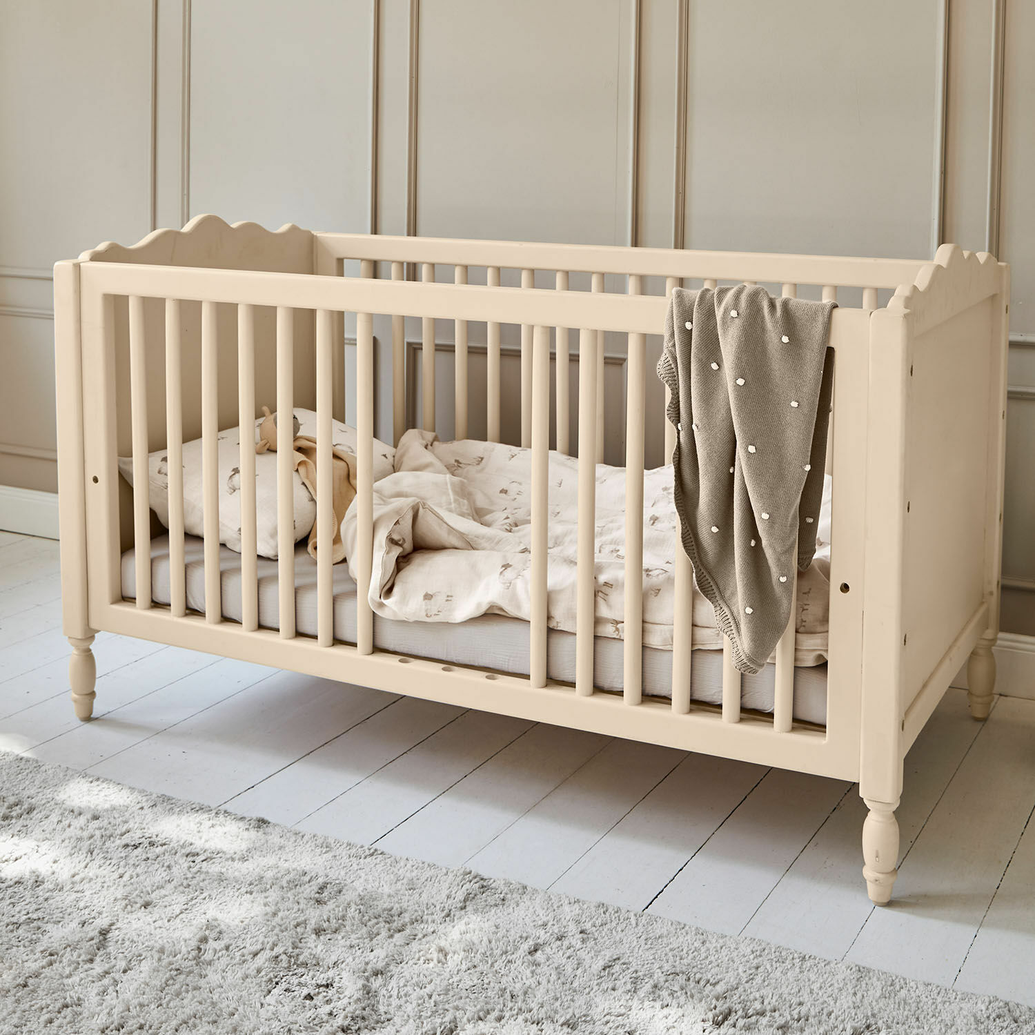 Lit bébé Arlithia Lit bébé en bois beige avec literie et couverture grise dans une chambre d'enfant lumineuse