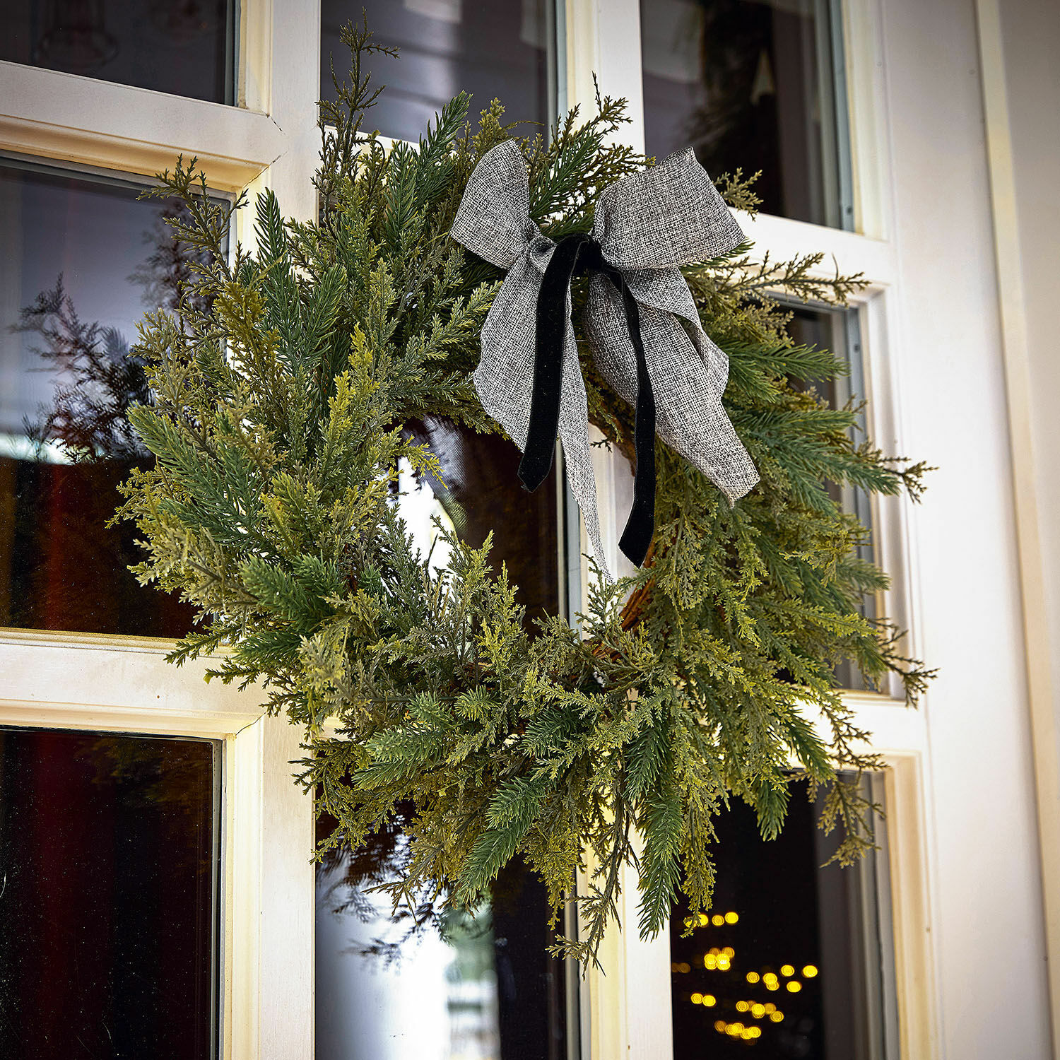 Couronne Julien Couronne de Noël en branches vertes avec un nœud gris sur une porte blanche