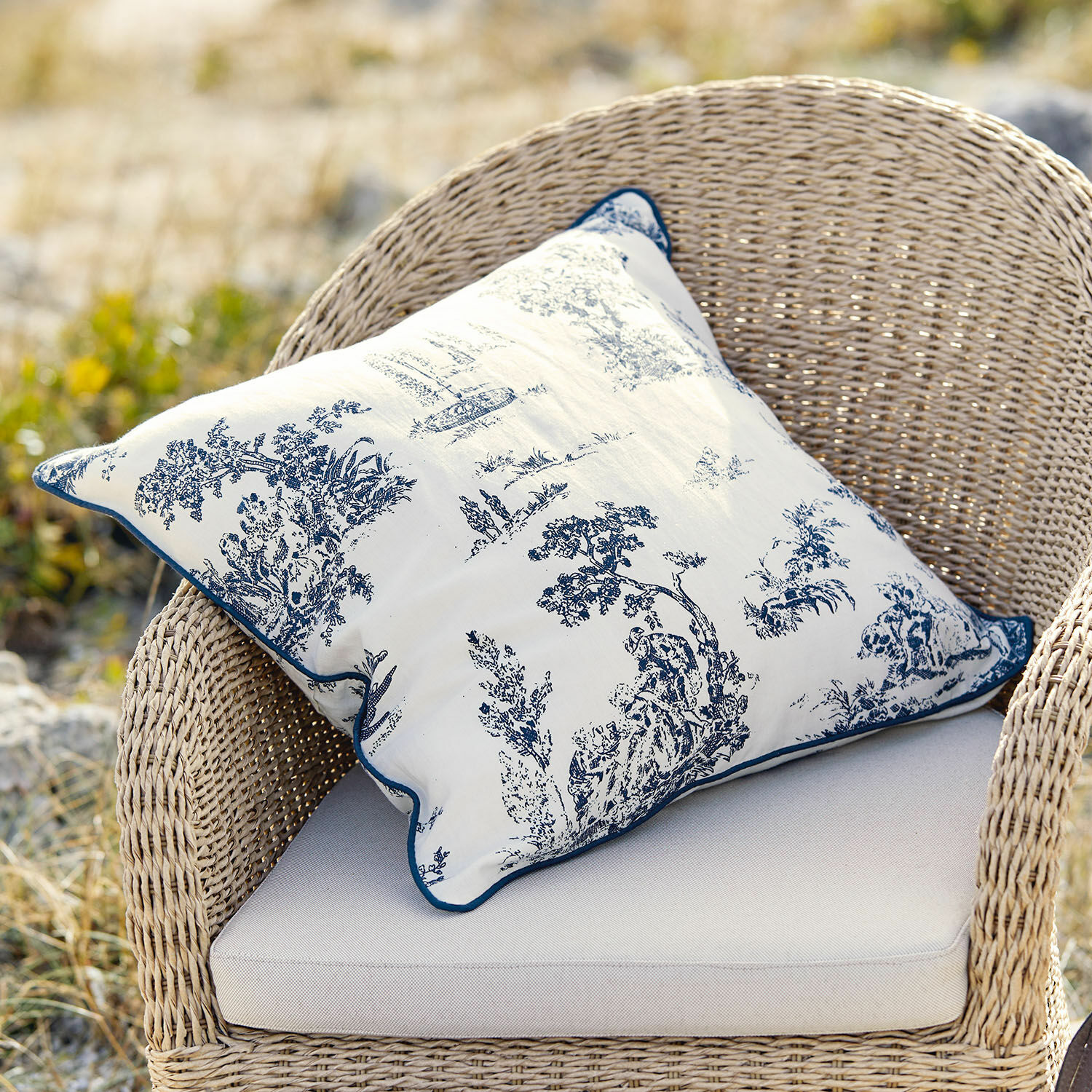 Housse de coussin Simone Coussin décoratif en coton blanc avec motif bleu classique sur fauteuil en osier beige