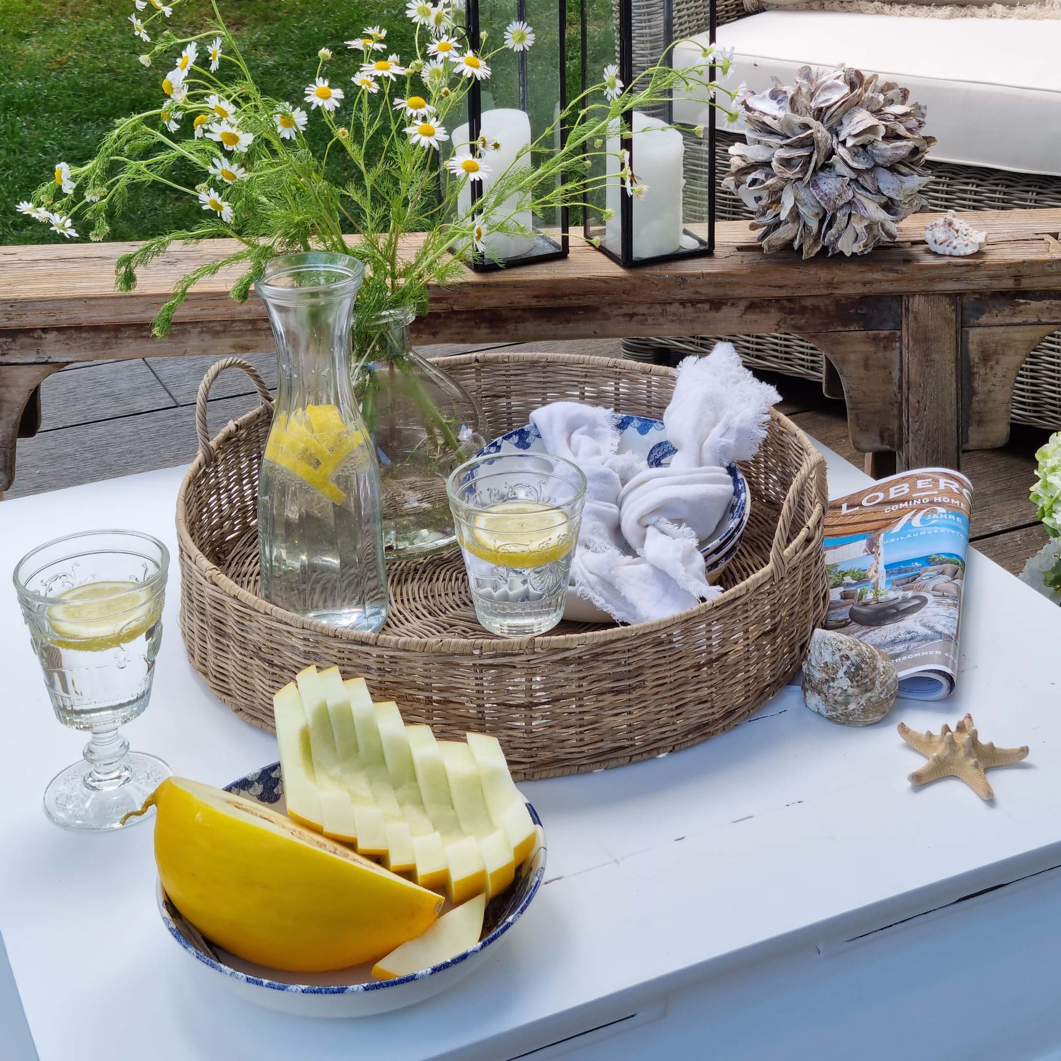 Panier rond en osier avec carafe d'eau citronnée et verre sur table blanche en jardin