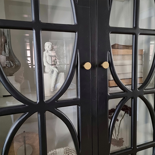 Armoire noire en métal avec motif décoratif et portes vitrées, décorations visibles à l'intérieur
