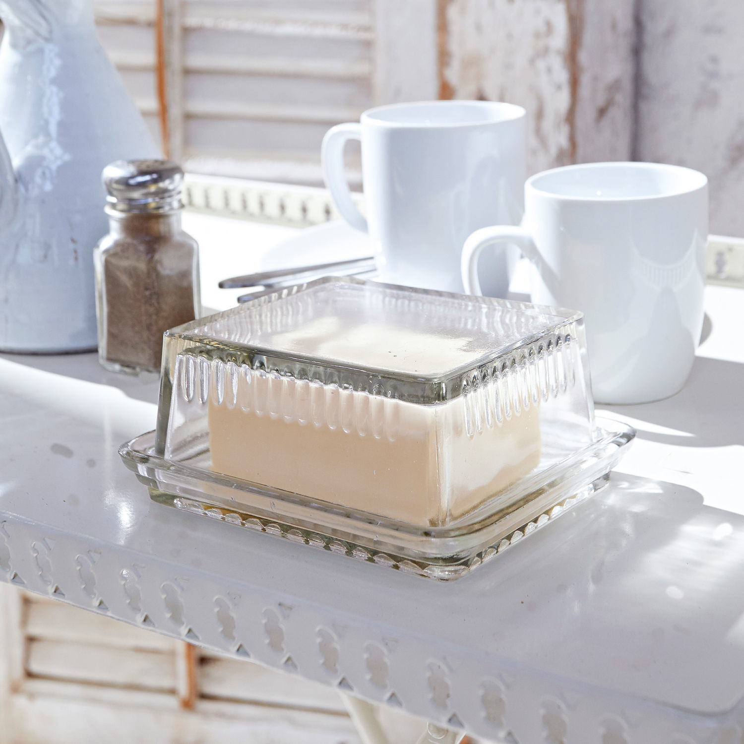 Beurrier Durham Beurrier en verre transparent avec couvercle sur table blanche avec tasses et salière
