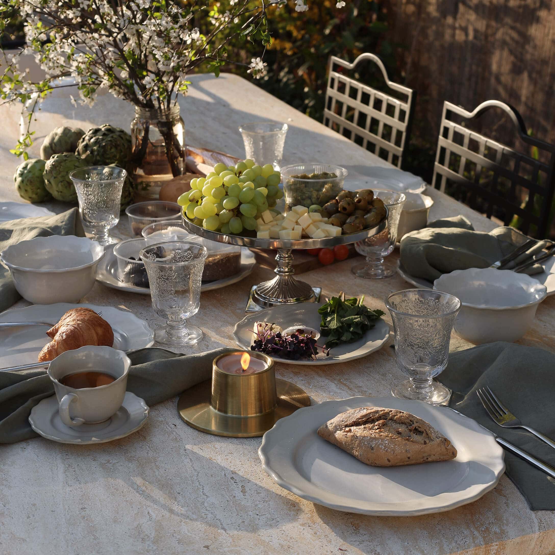 Table en pierre avec vaisselle blanche, bougie et plateau de raisins, fromage et olives en extérieur