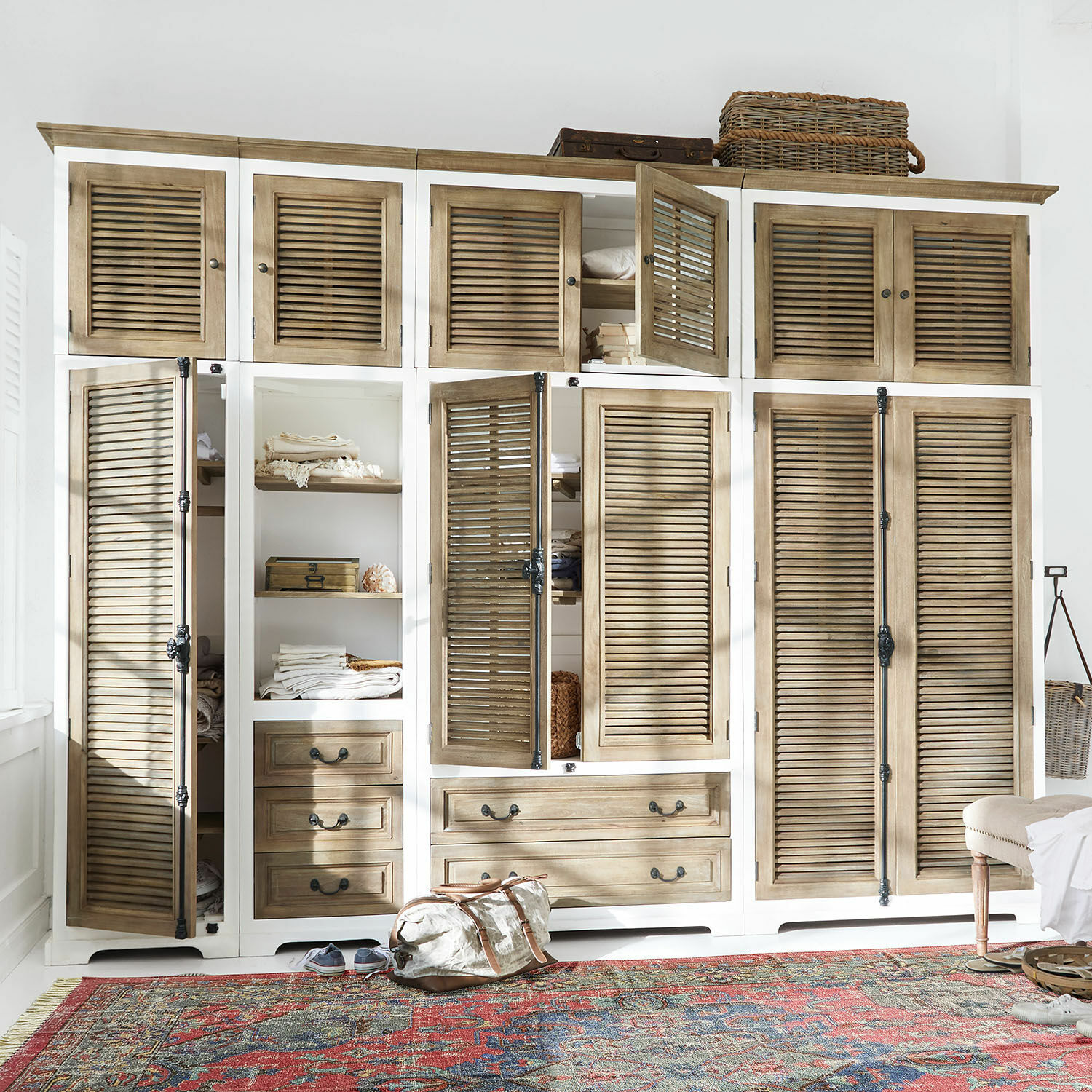 Dressing Daviau Grande armoire en bois blanc et naturel avec portes à persiennes et tiroirs, posée sur un tapis coloré.
