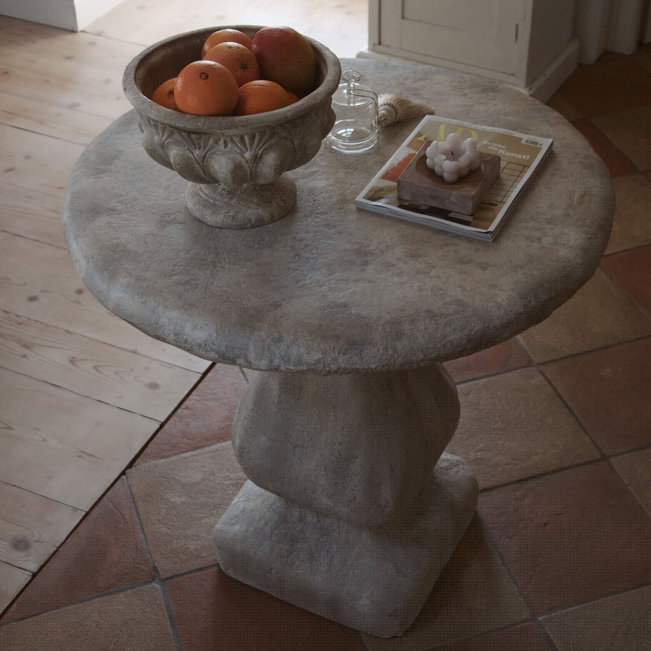 Table ronde en pierre grise avec un bol de fruits et des objets décoratifs sur le dessus