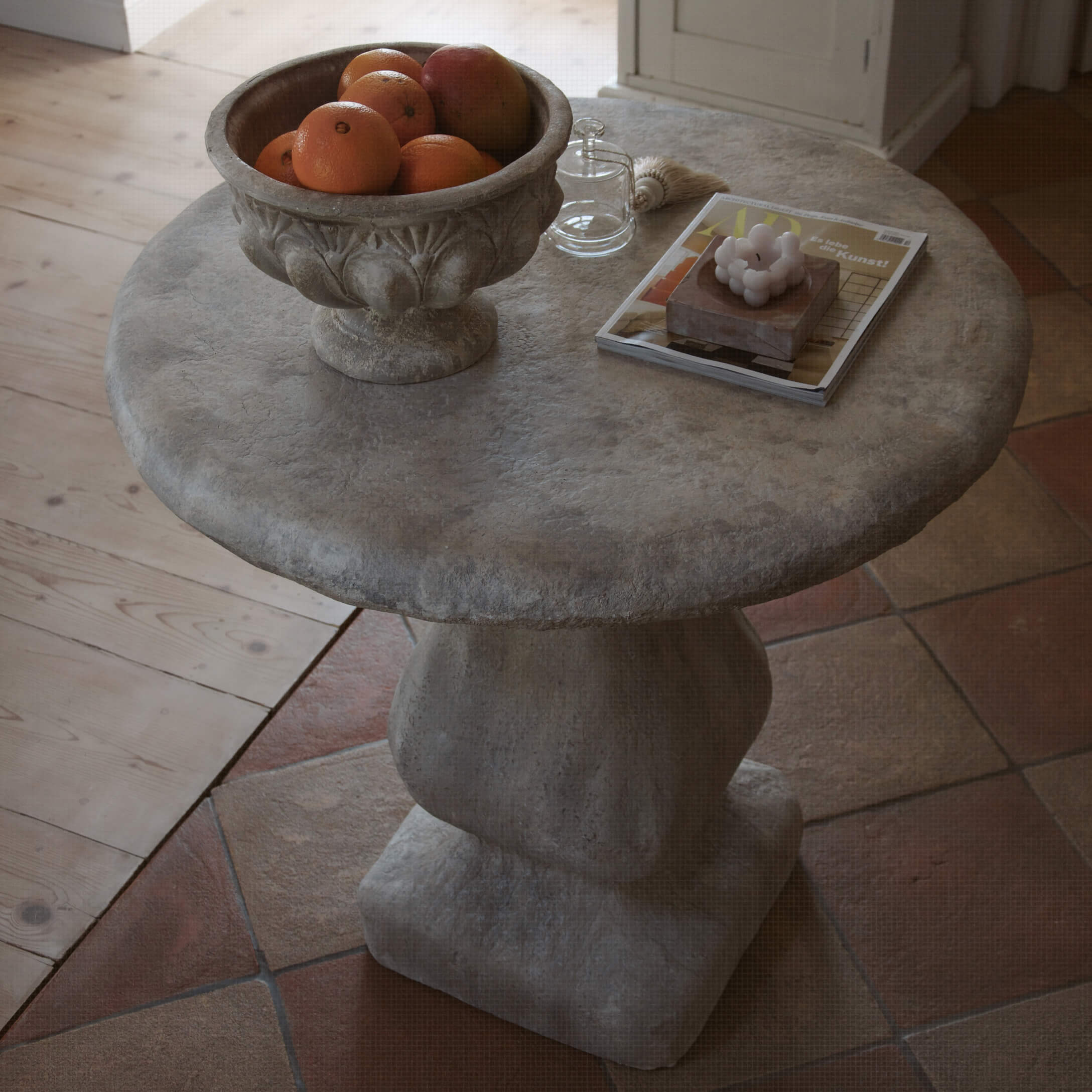 Table ronde en pierre grise avec un bol de fruits et des objets décoratifs sur le dessus