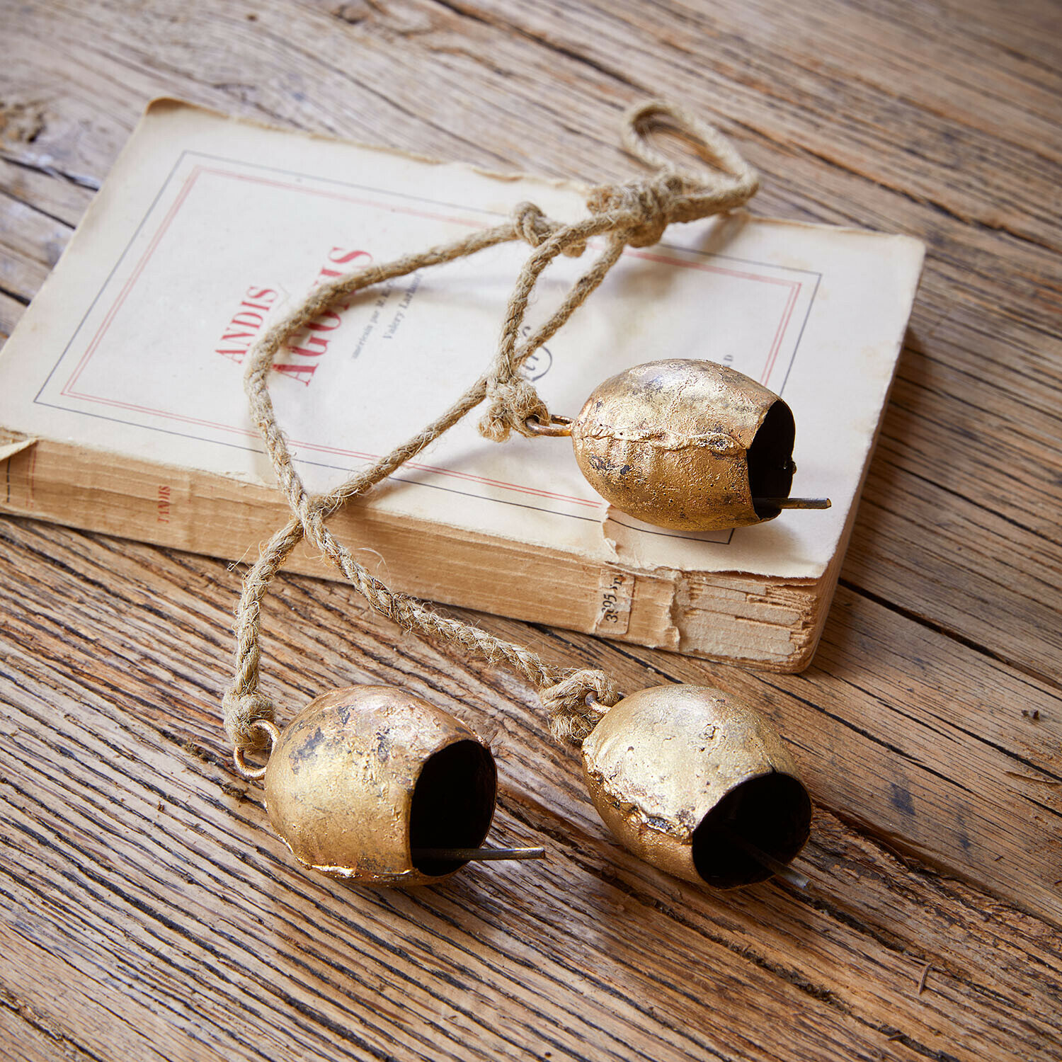 Lot de 3 cloches Orelli Trois cloches en métal doré sur une corde posées sur une table en bois avec un livre ancien
