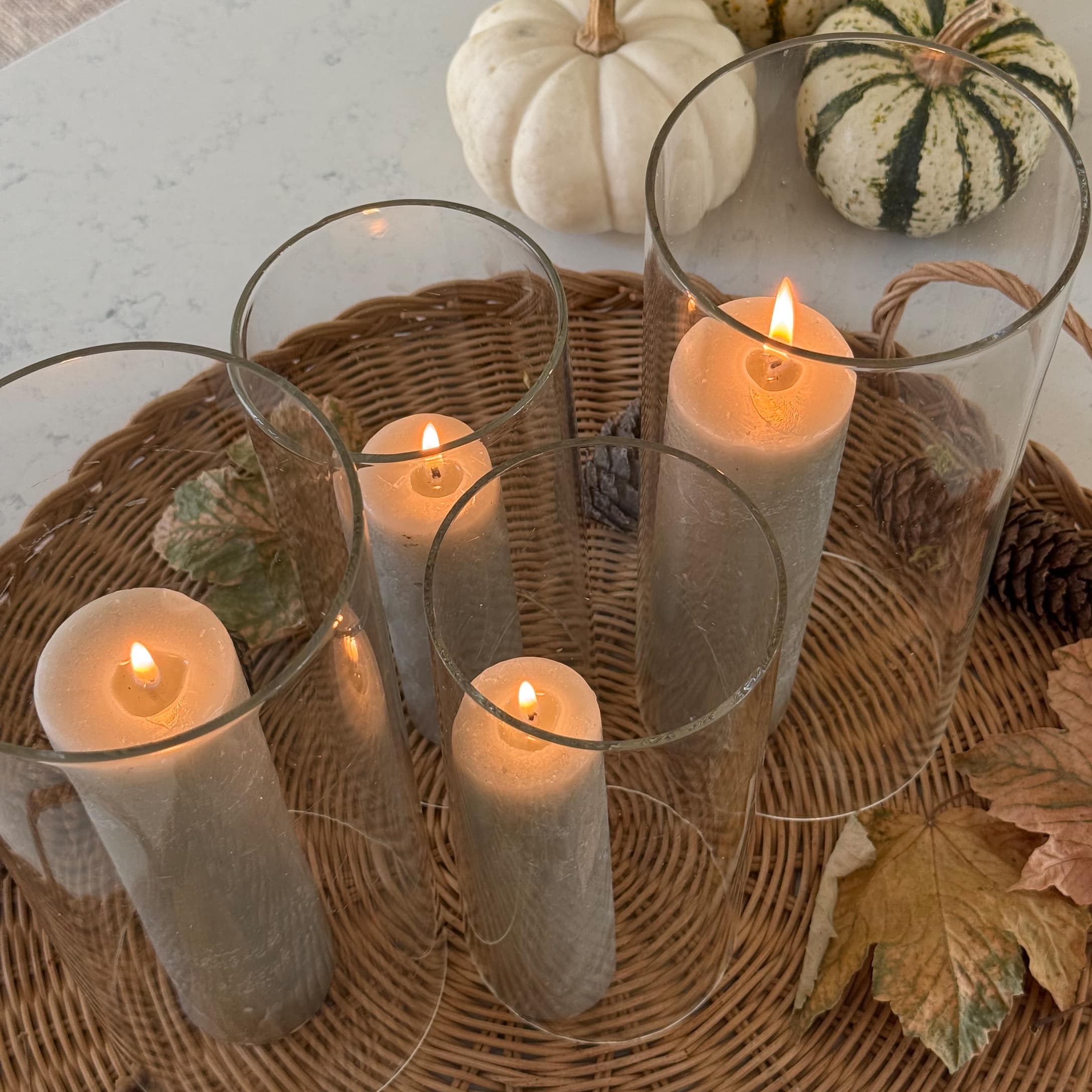 Ensemble de bougies grises dans des photophores en verre sur un plateau en osier avec décorations d'automne