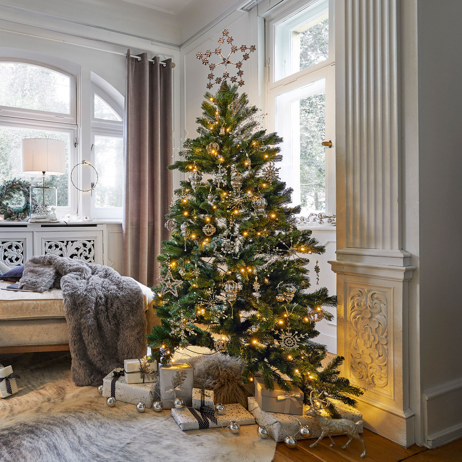 Sapin de Noël Helford Sapin de Noël vert décoré d'ornements dorés et lumières dans un salon lumineux avec cadeaux