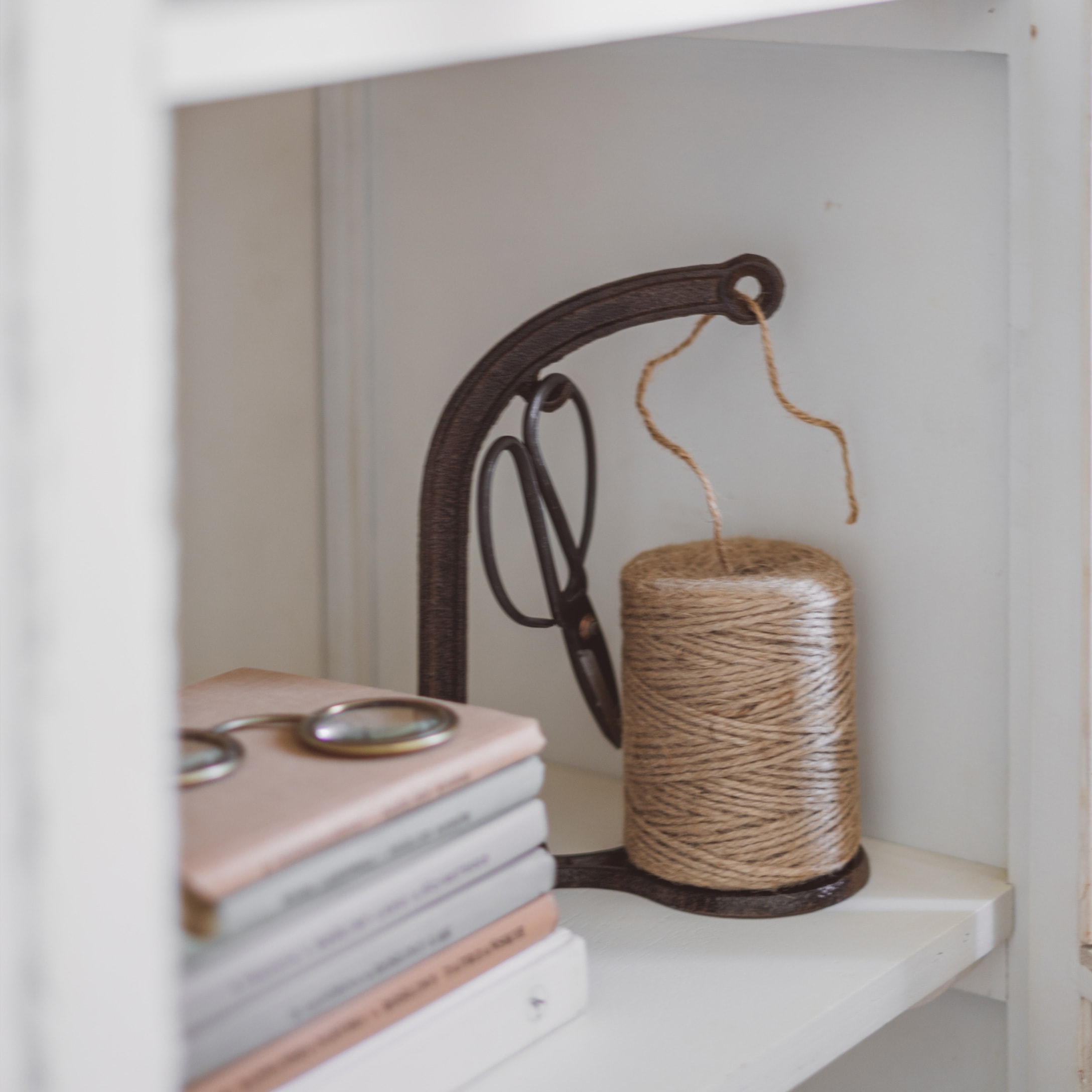 Support en métal avec bobine de ficelle beige et ciseaux sur étagère blanche avec livres