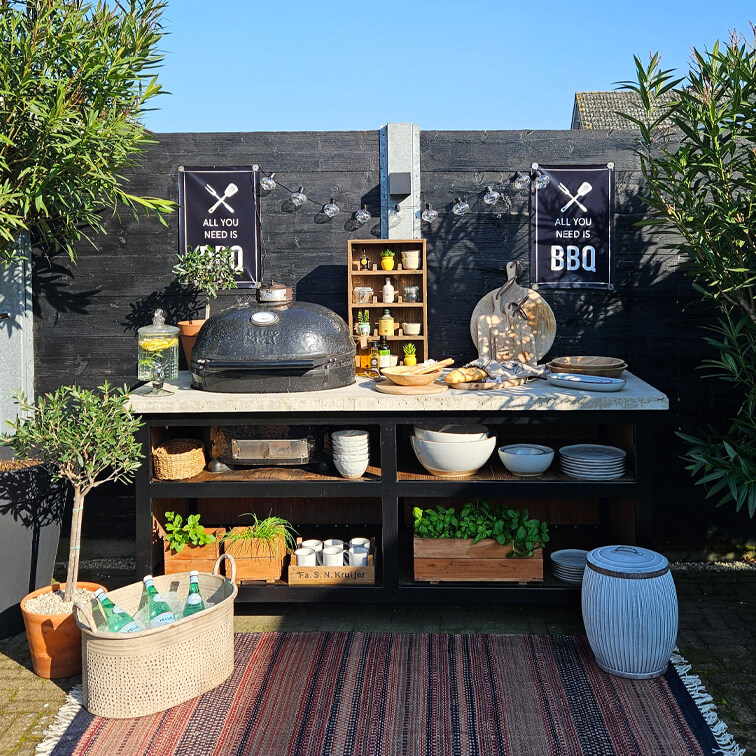 Espace barbecue extérieur avec grill noir, plan de travail blanc, plantes en pot et accessoires de cuisine