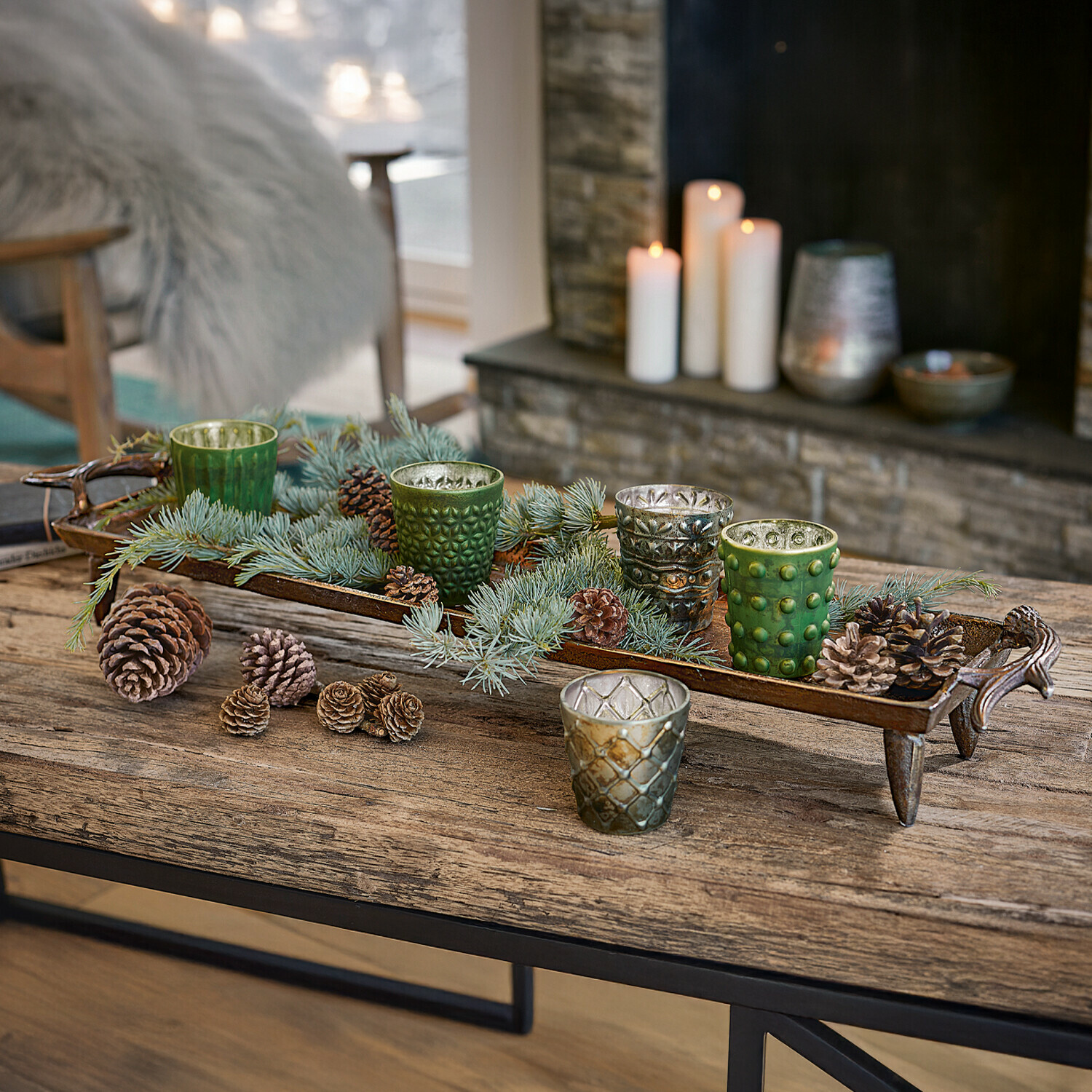 Plateau Donia Plateau décoratif en métal avec bougeoirs en verre verts et argentés et pommes de pin sur table en bois