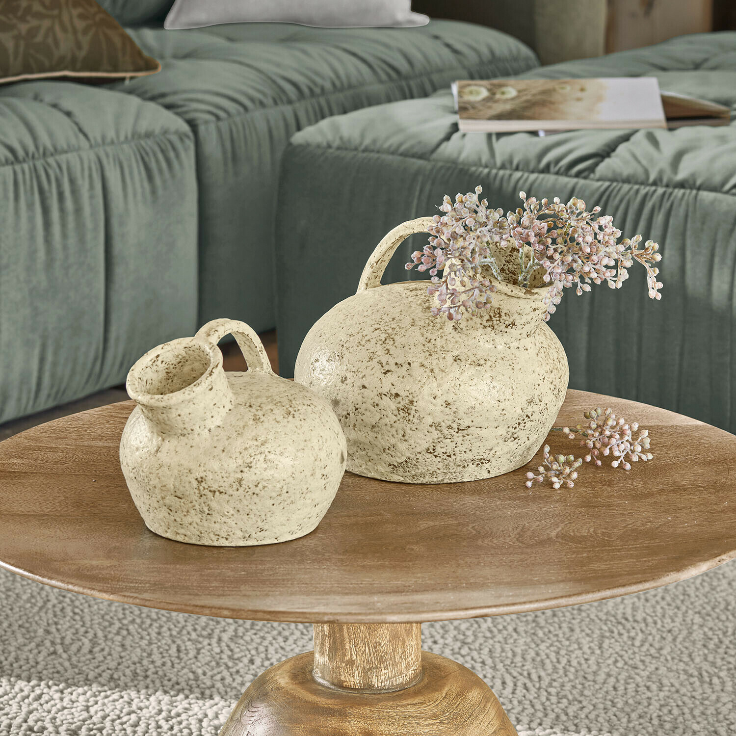 Vase 2er Set Gravière Deux vases en céramique crème avec anses sur une table en bois devant un canapé vert dans un salon